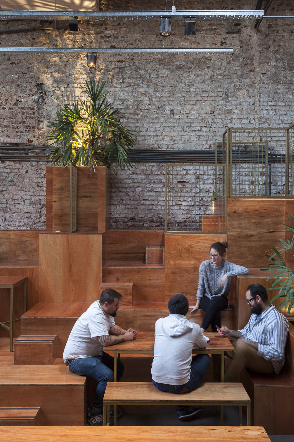 Four people talking around a wooden table on the terraced plywood steps, a palm lit by a spotlight behind them