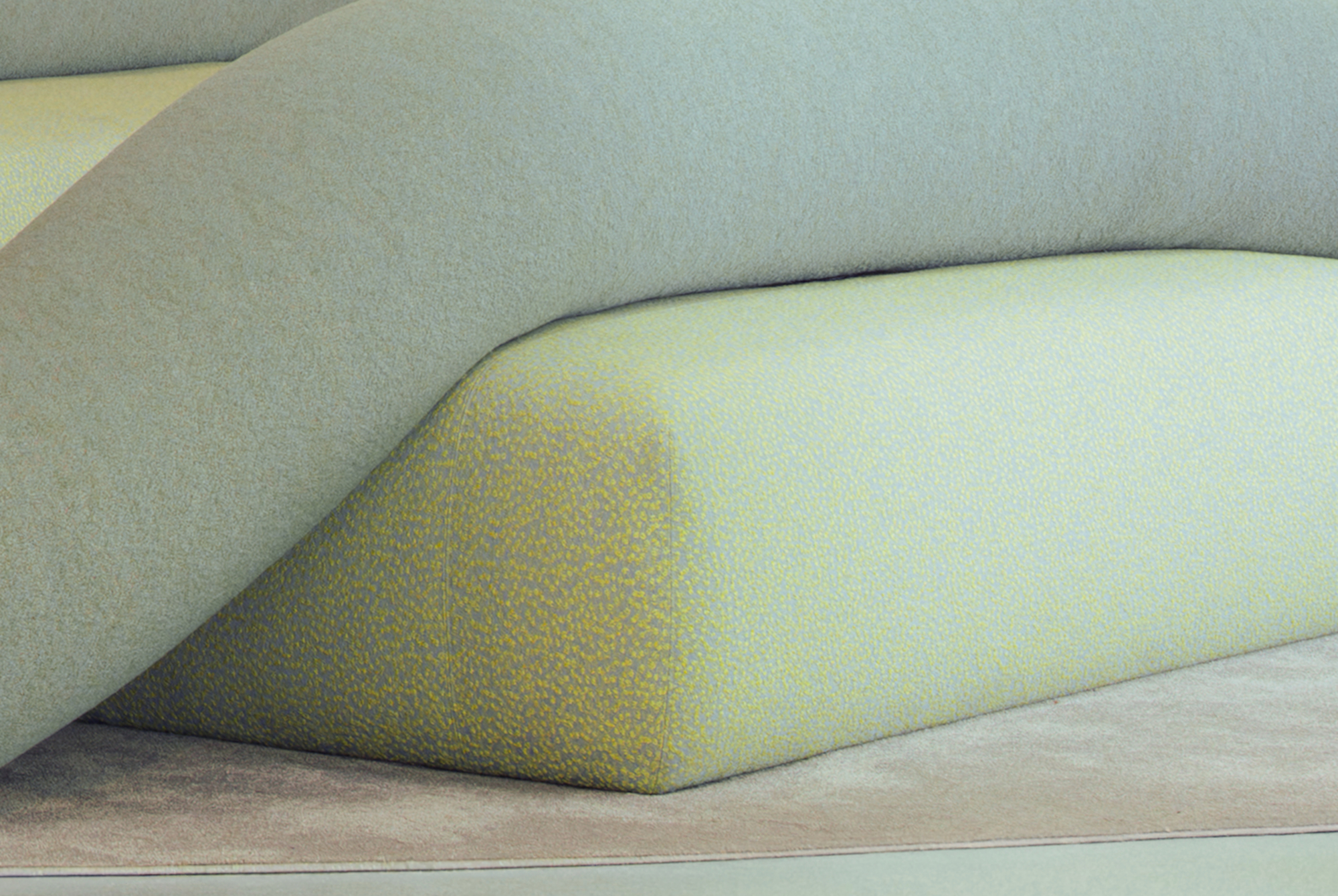 Close-up of a soft green upholstered cushion with a yellow speckled fabric, tucked beneath a curving felt-like bolster in diffuse light