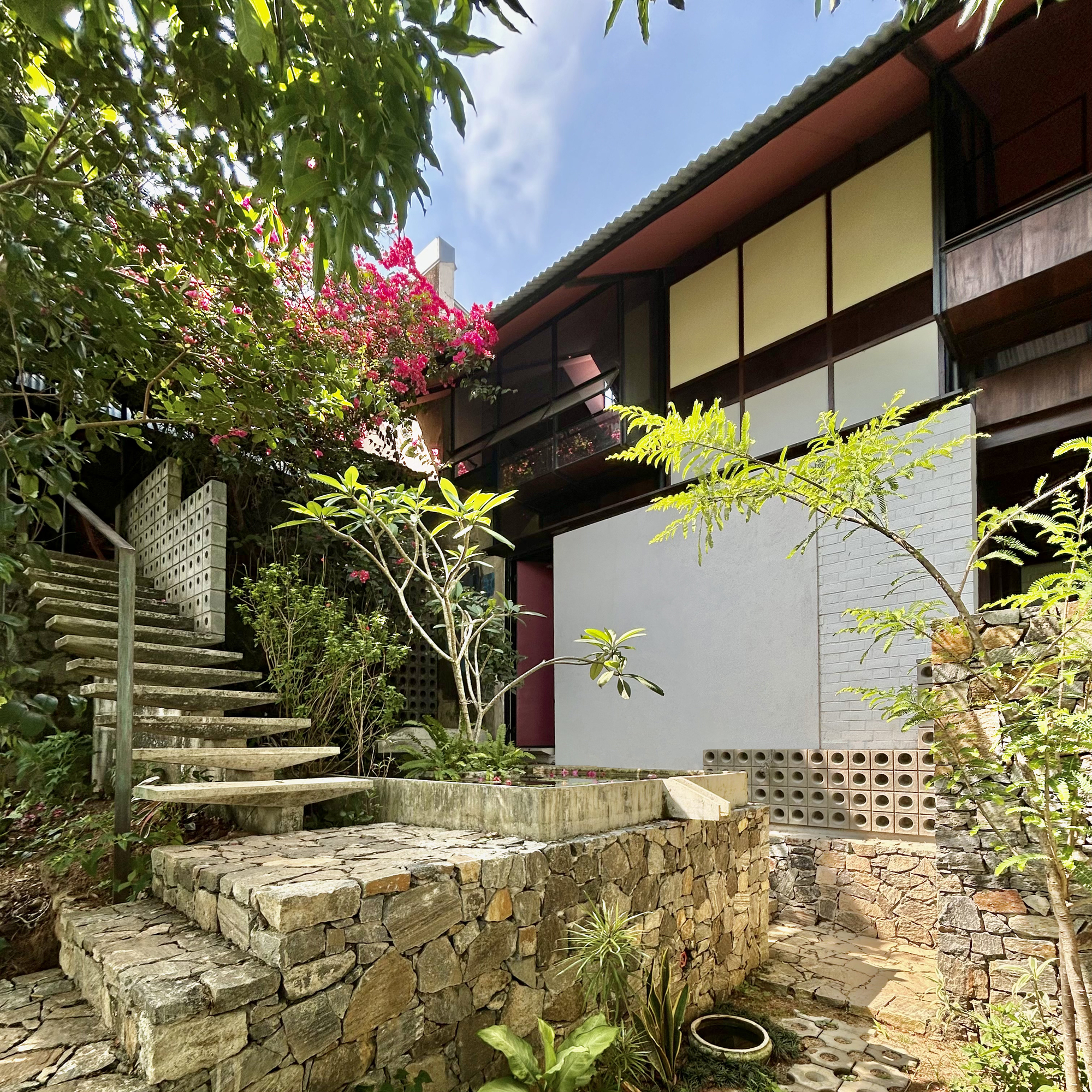 Stone retaining wall and floating concrete stair beside a white-rendered wall, with bougainvillea blooming under a blue sky