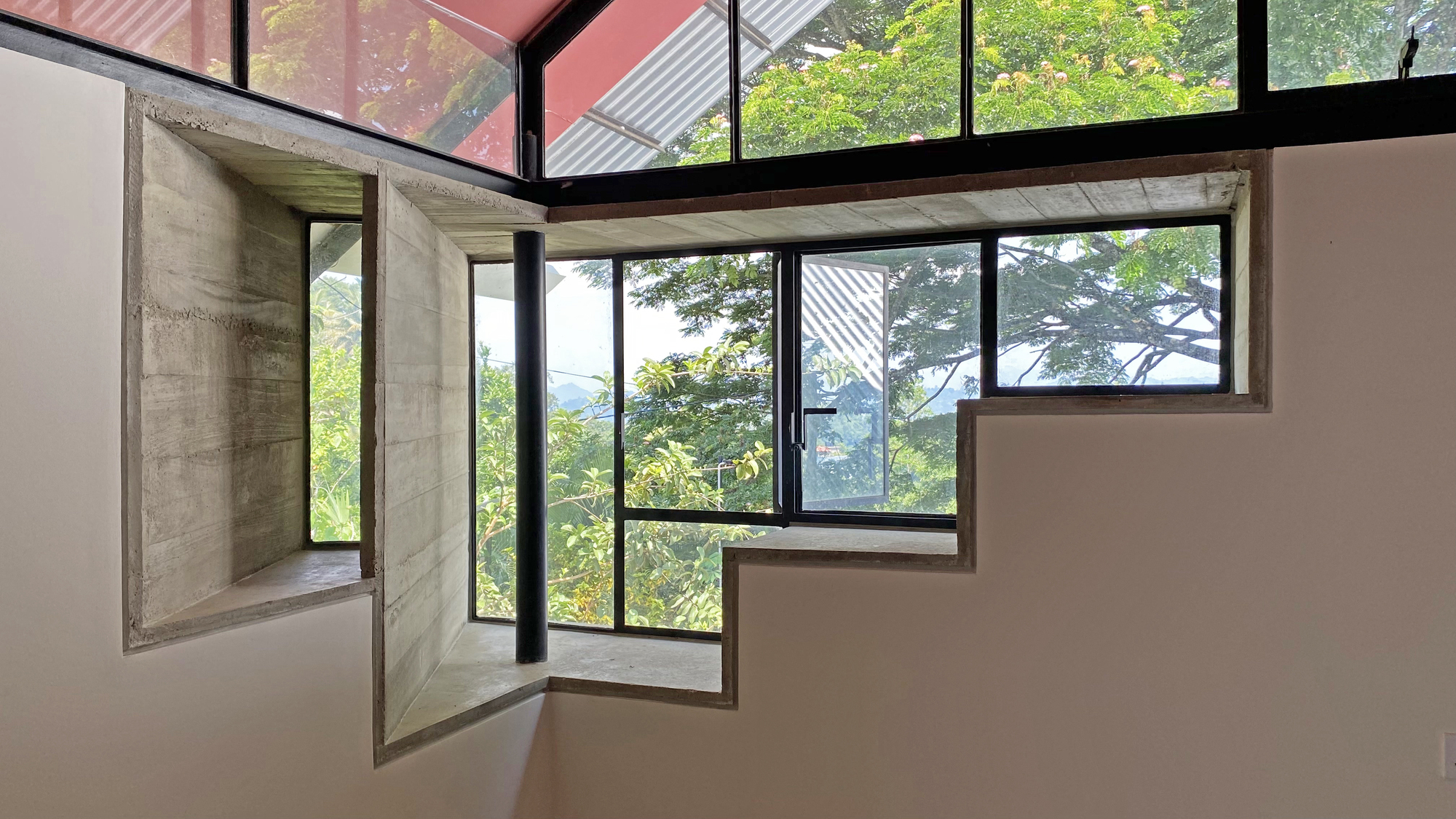 Board-formed concrete window niches stepping along a pale stair wall, with green treetops visible through black-framed glazing