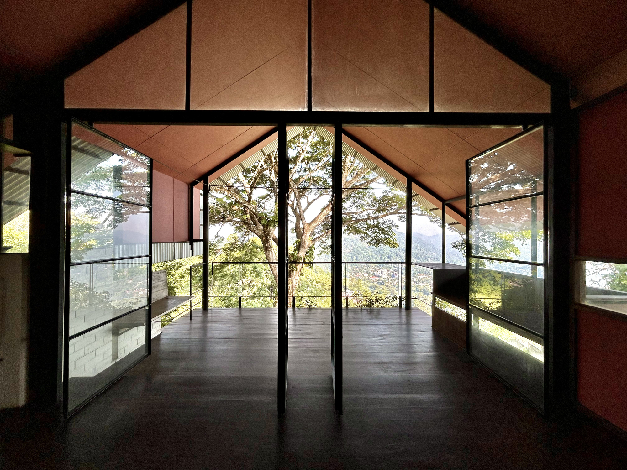 Gabled upper room with steel-framed glass doors opening onto a deck and a large tree against distant hills