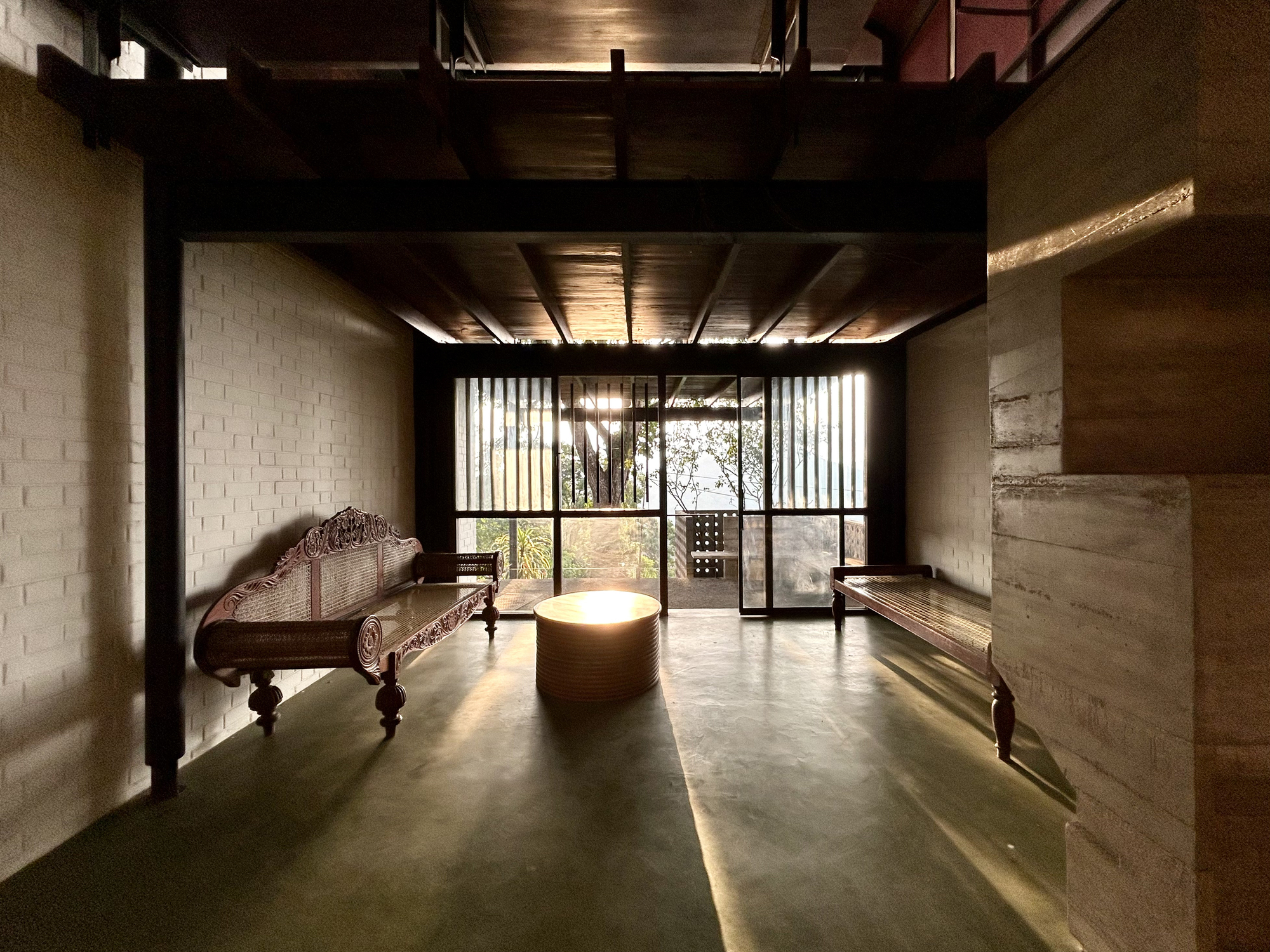 Dim ground-floor room with carved wooden benches, brick walls and green floor, backlit by slatted glazing at the far end