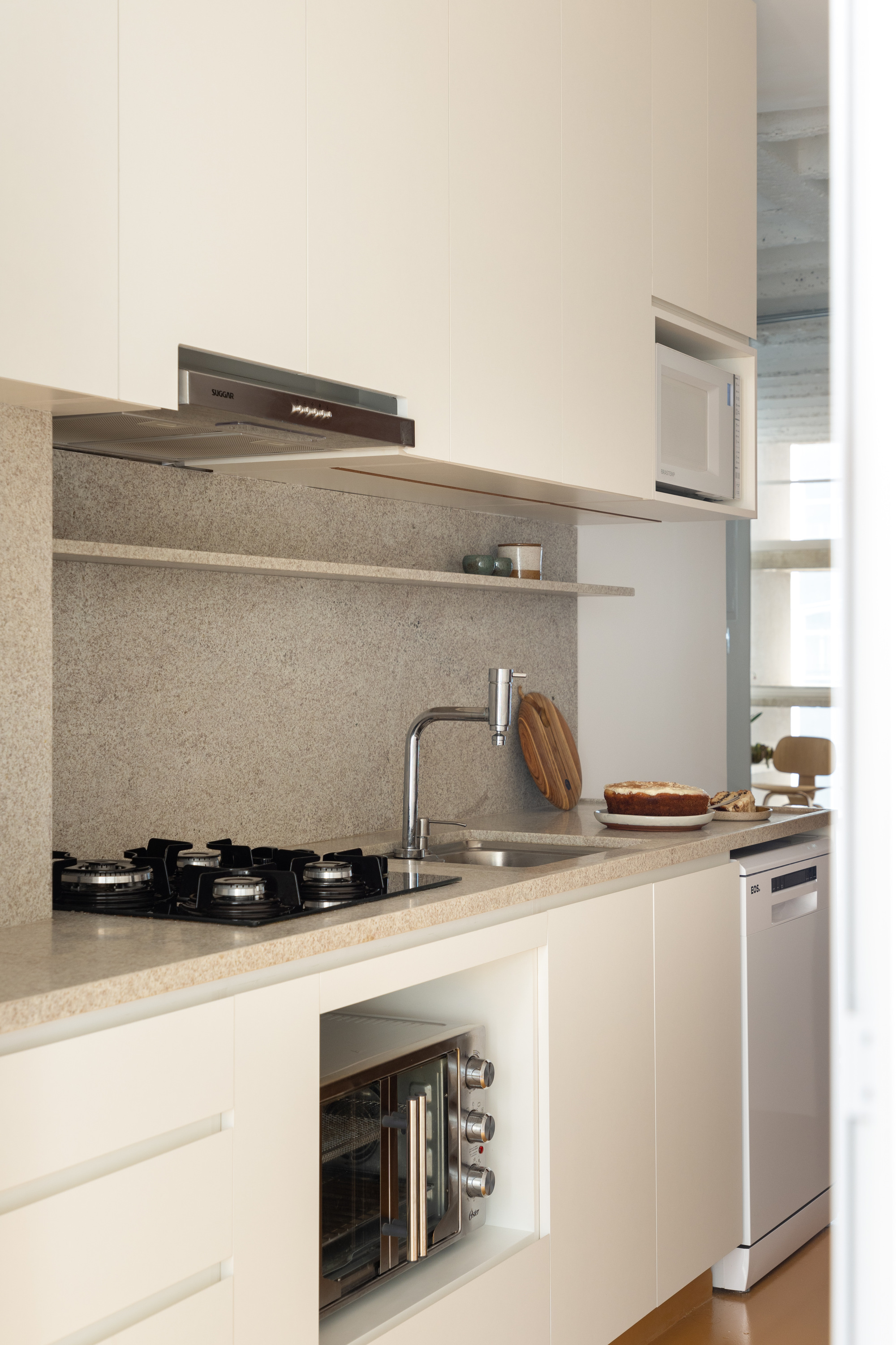 Galley kitchen with cream cabinets, a speckled stone backsplash, a gas hob and a steel faucet, with a cake on the counter
