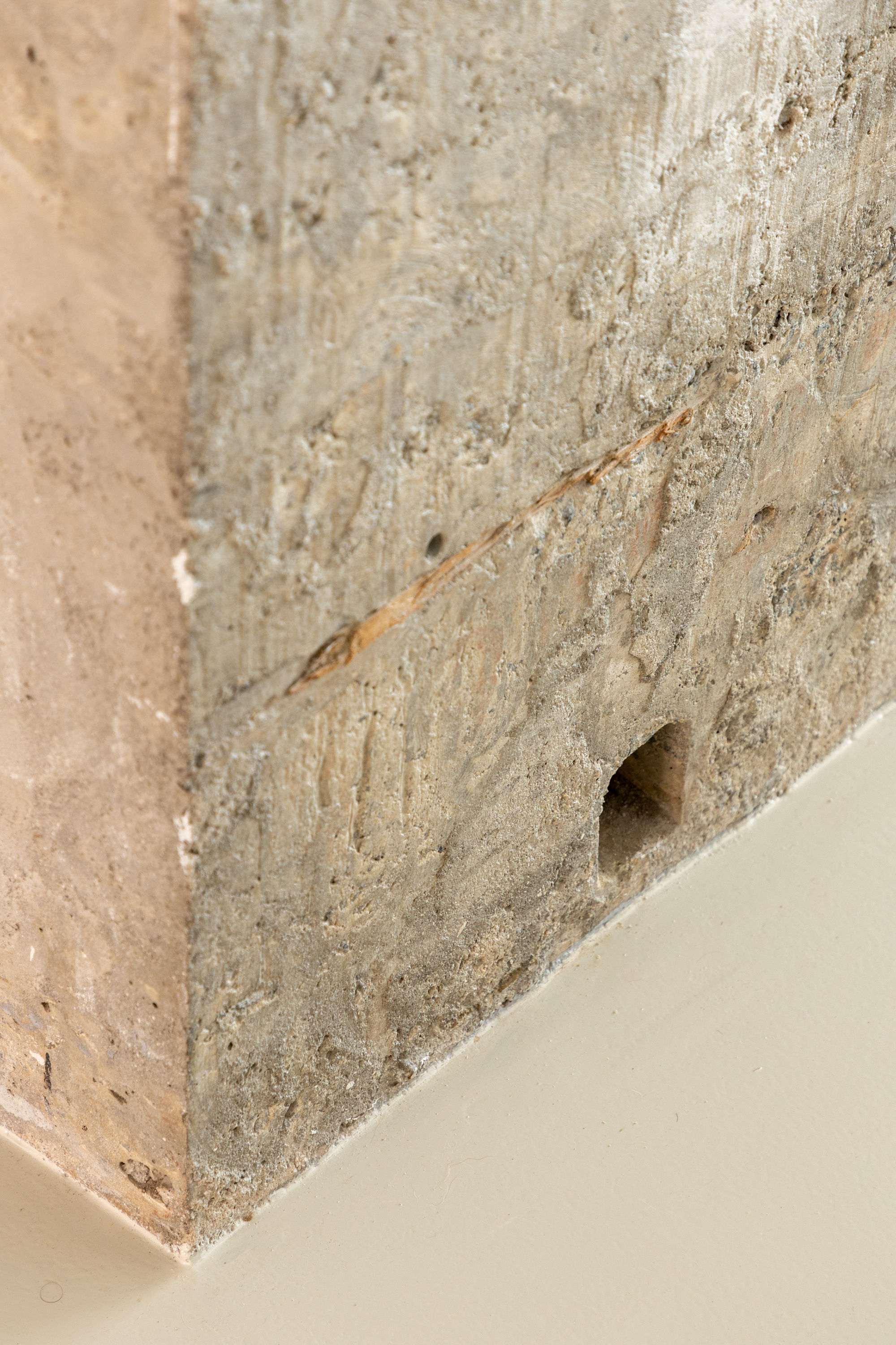 Close-up of the rough board-marked concrete column base meeting the cream resin floor, with a small hole and rust stain
