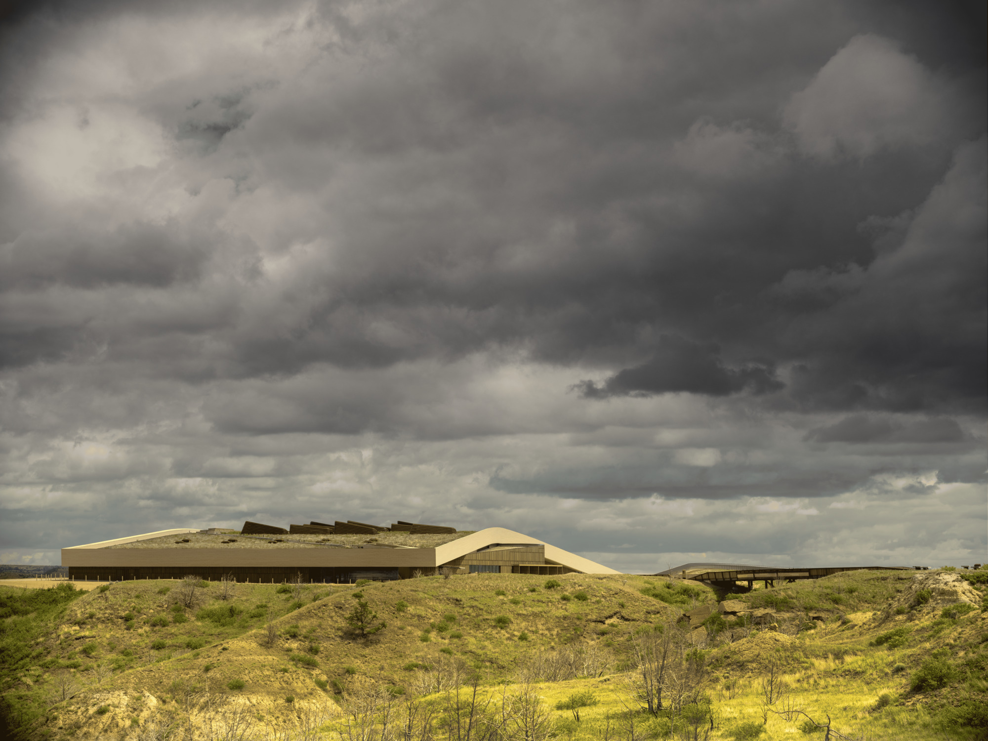 Low long building with a pale curved roof edge sitting on a grassy badlands ridge under heavy storm clouds