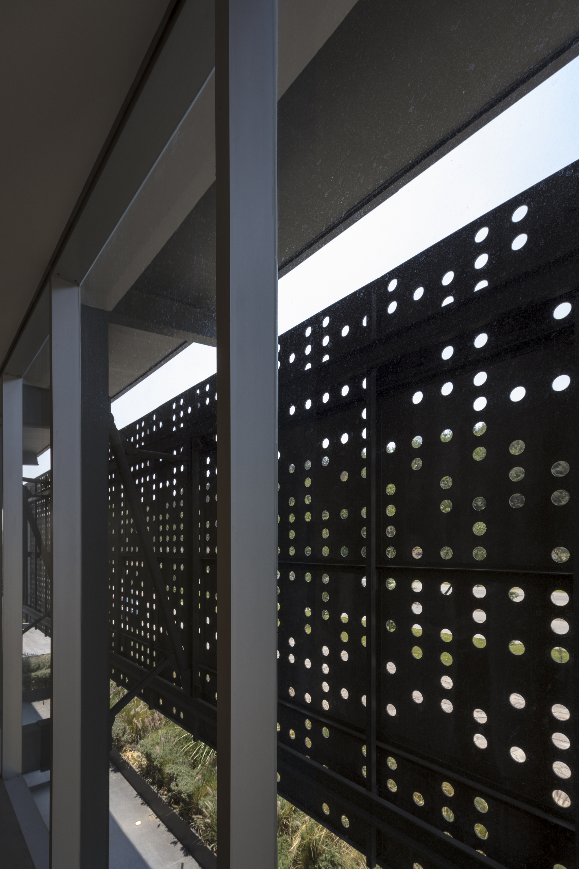 View from inside along a steel column to the perforated screen, with daylight passing through the round holes