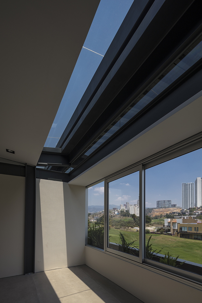 Interior corner with a skylight strip and sliding window framing a green lawn and distant towers under blue sky