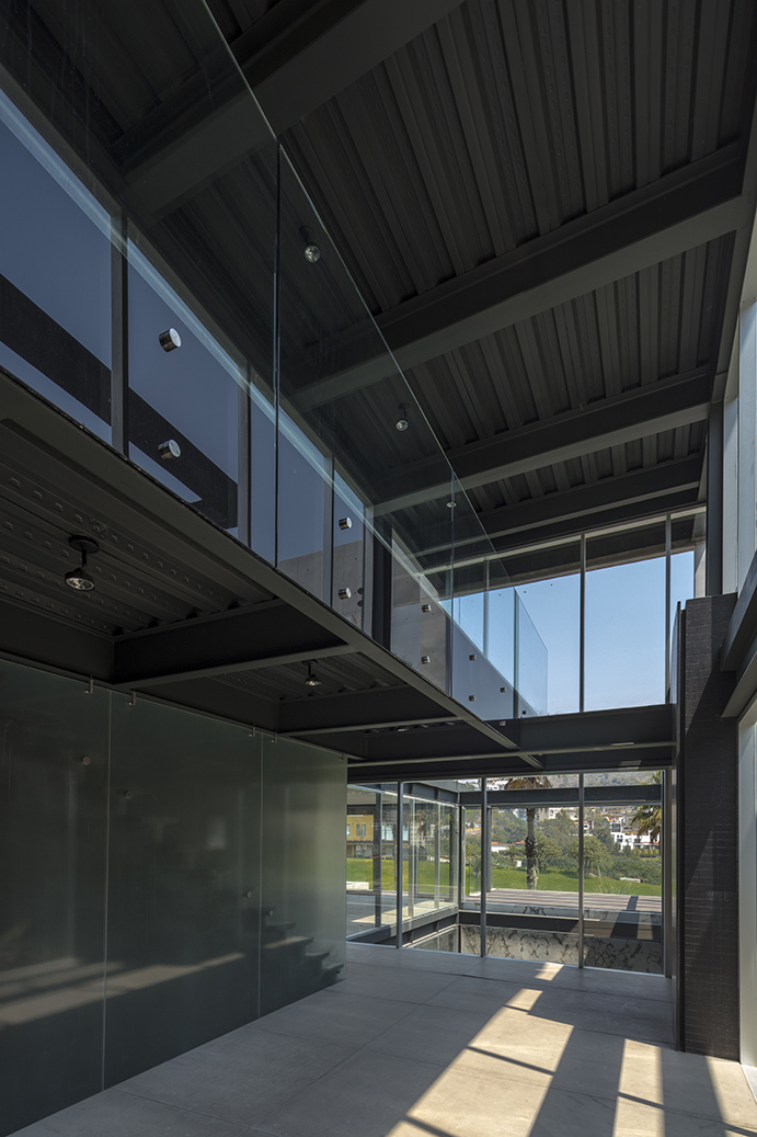 Double-height hall with exposed steel beams, a glass balustrade on the mezzanine and sunlit concrete floor