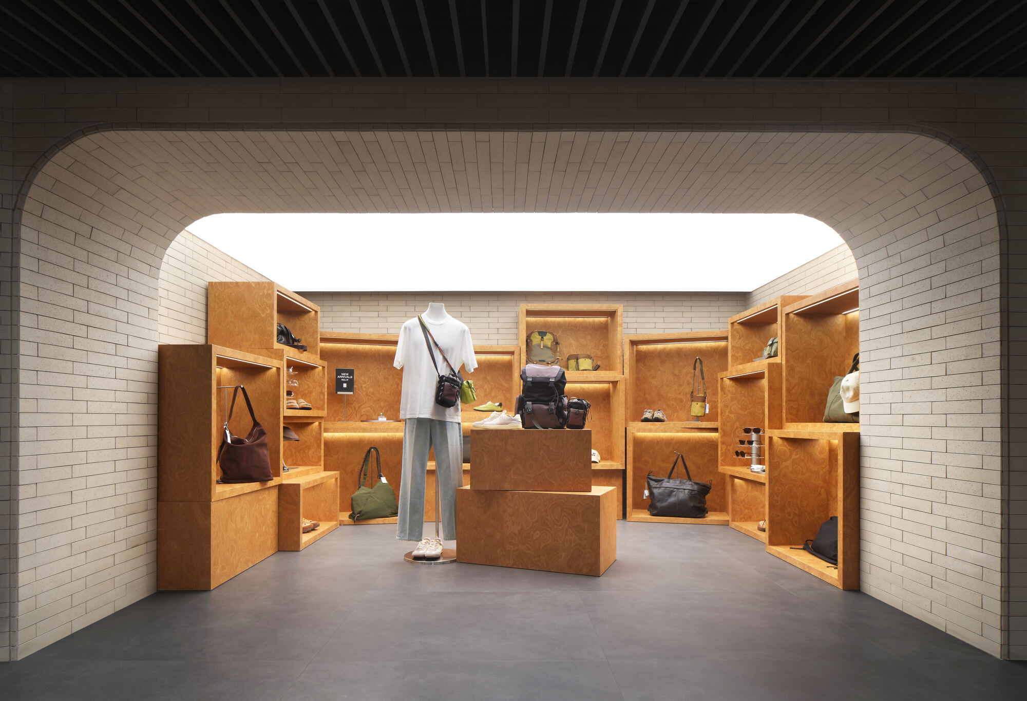 Accessories display room with cork-toned shelving boxes and a mannequin, framed by an arched white brick opening and glowing ceiling panel