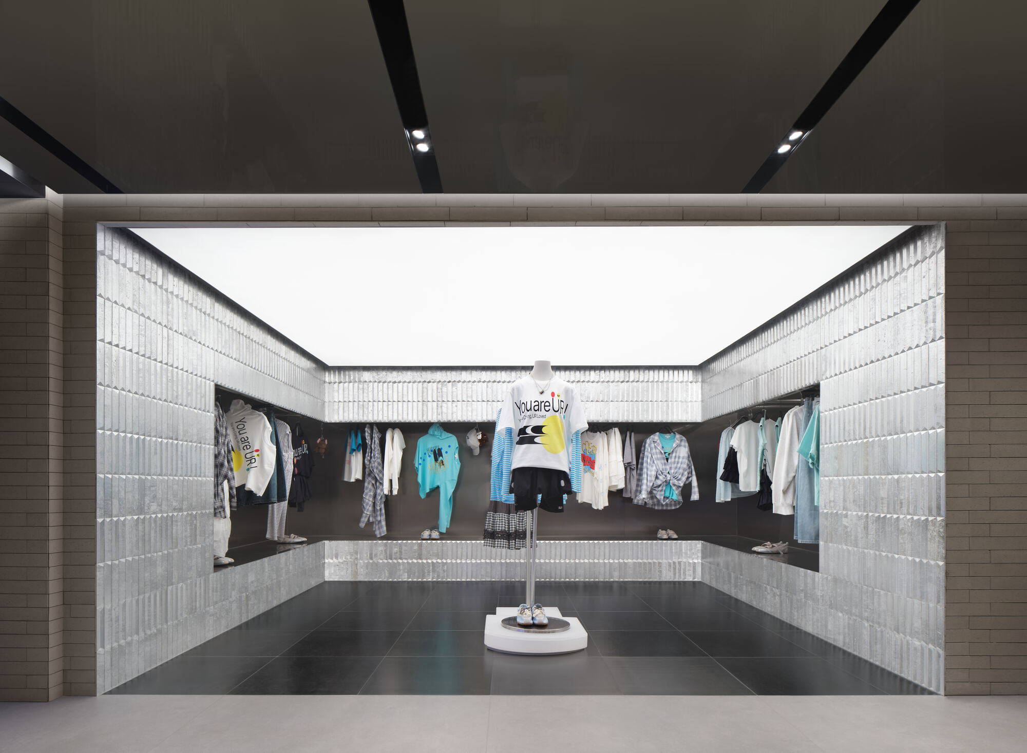 Alcove lined with galvanized metal tiles, with a mannequin and hanging clothes on a dark tiled floor under a white light ceiling