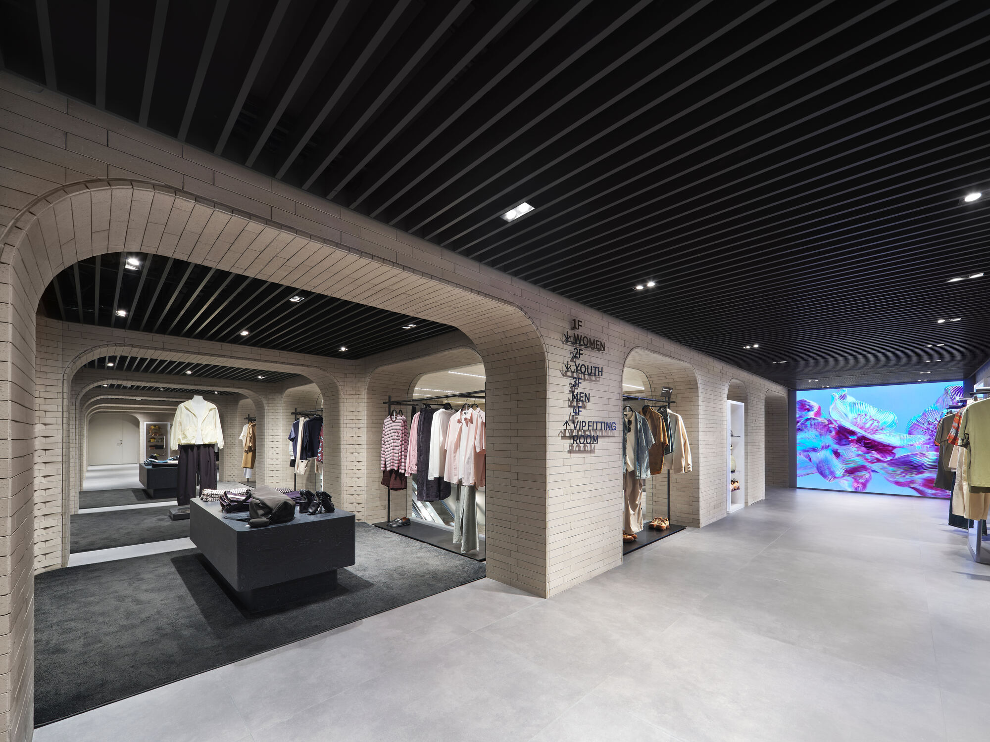 Row of pale brick arches in a clothing store with a black slatted ceiling and a bright floral video screen at the end