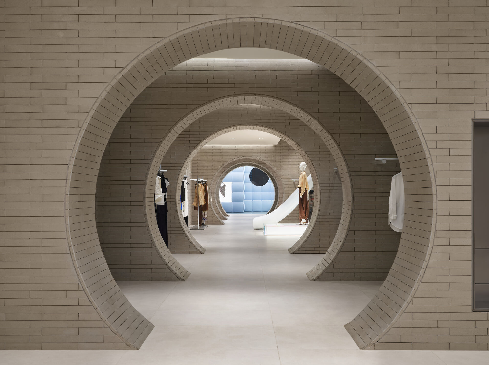 Nested circular brick portals framing a view down the shop floor toward a mannequin and a blue padded wall