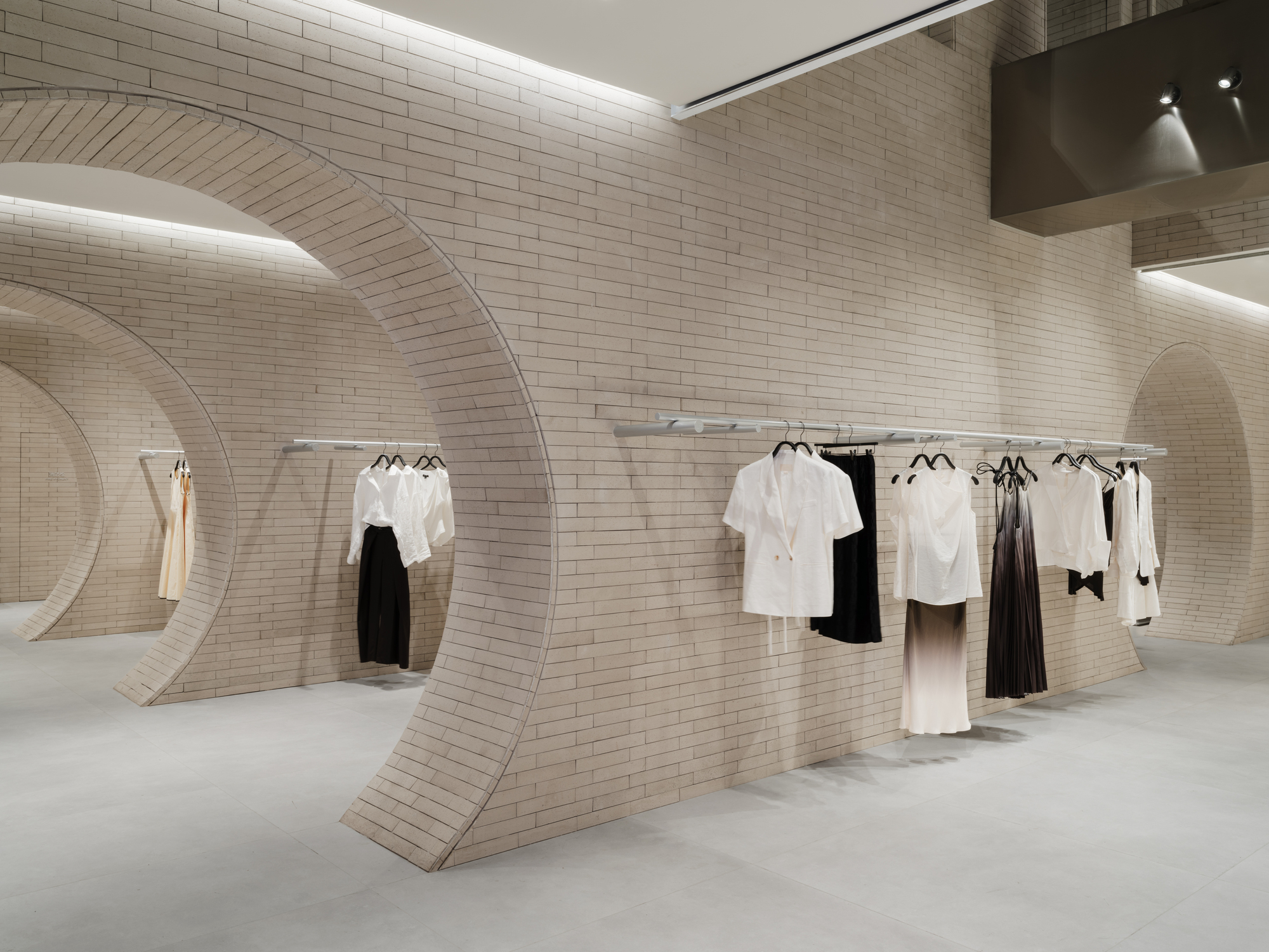 Curved brick wall with arched openings and a rail of white and black garments under soft cove lighting