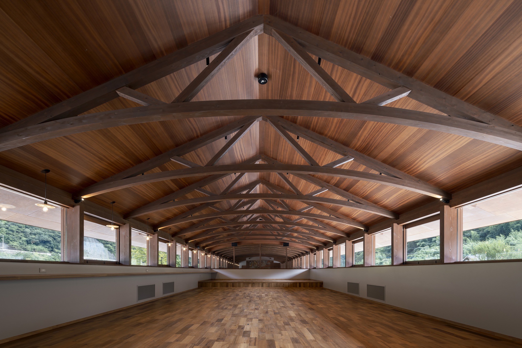 Interior of the long hall with arched timber trusses, cedar ceiling and wood parquet floor, clerestory windows showing trees