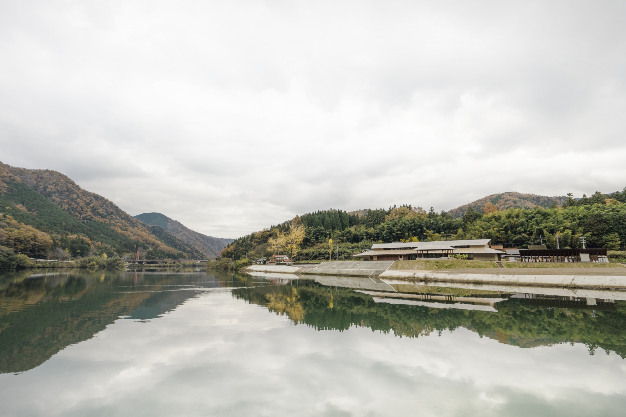 Low-slung roofed building on the far shore, mirrored in still lake water under an overcast autumn sky