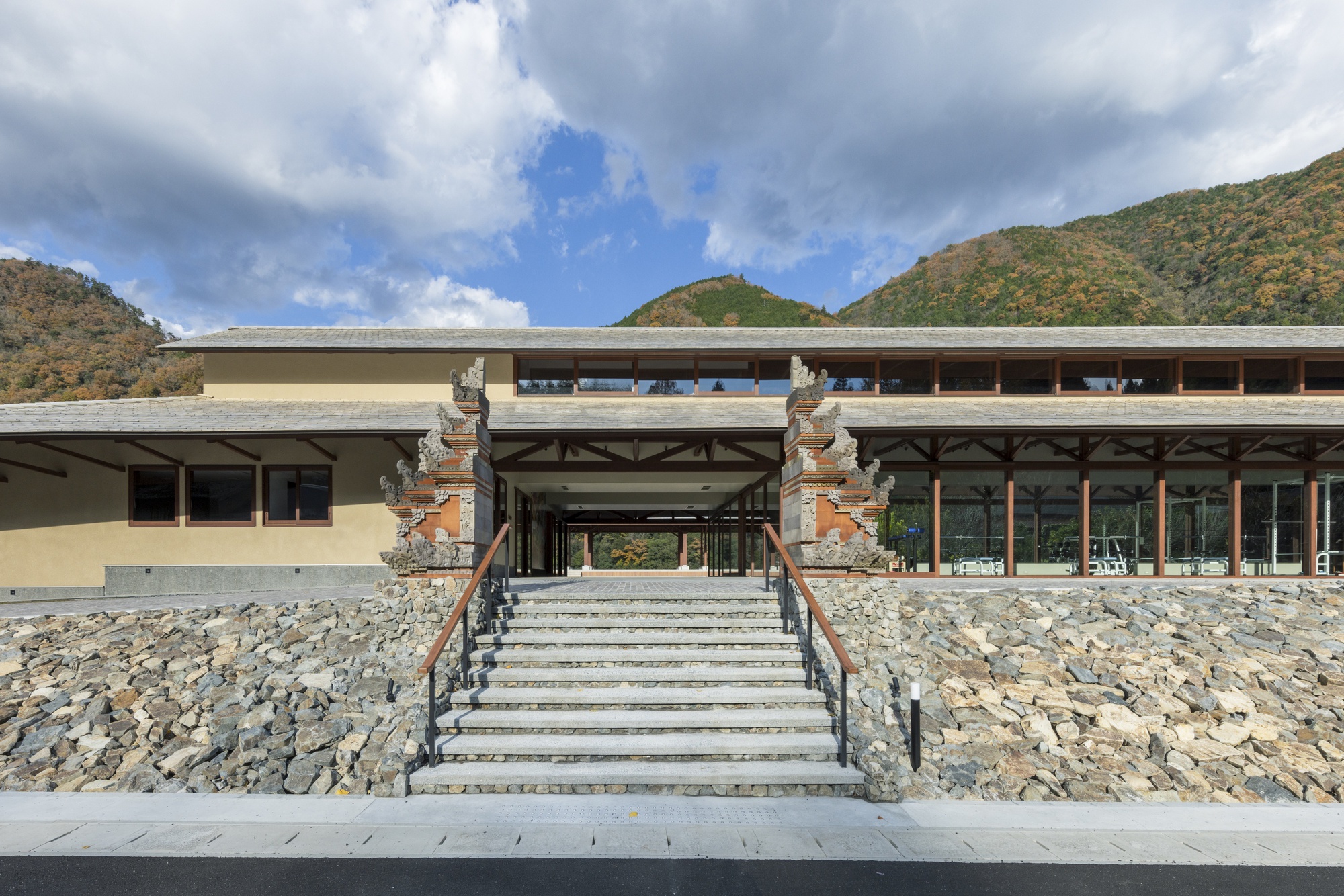 Frontal view of the central stone stair climbing between rubble banks to carved gate pillars and a timber-framed glazed hall