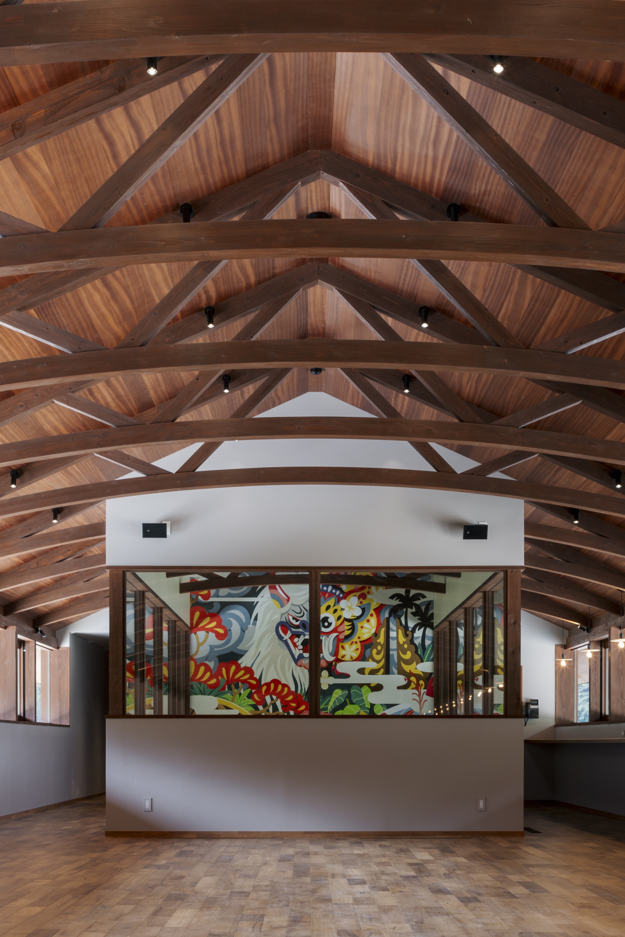 Arched timber trusses over a hall with a painted mural framed in a glazed opening, and a wood block floor below