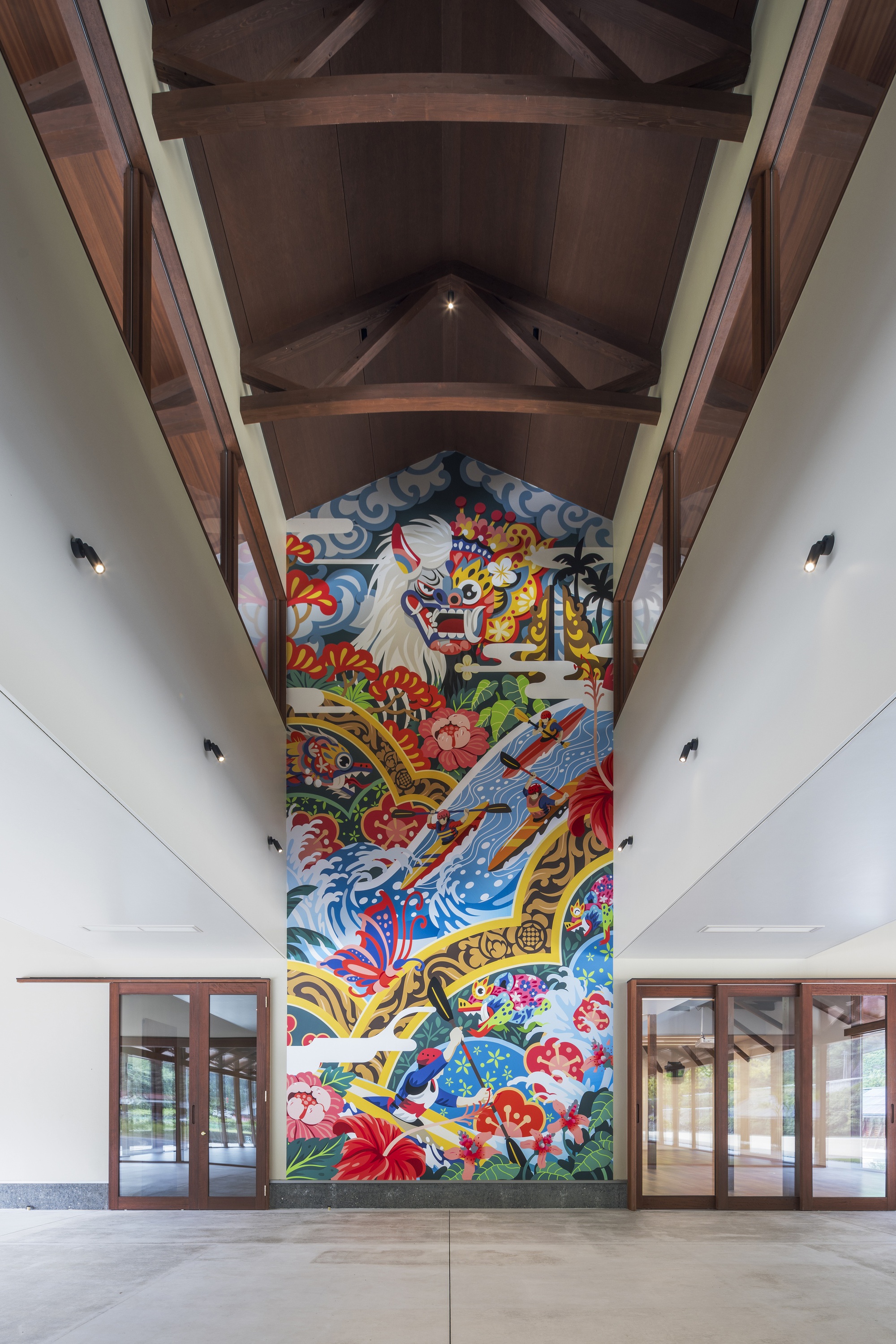 Double-height entrance hall with a tall colorful mural of a lion mask and waves beneath a timber truss ceiling