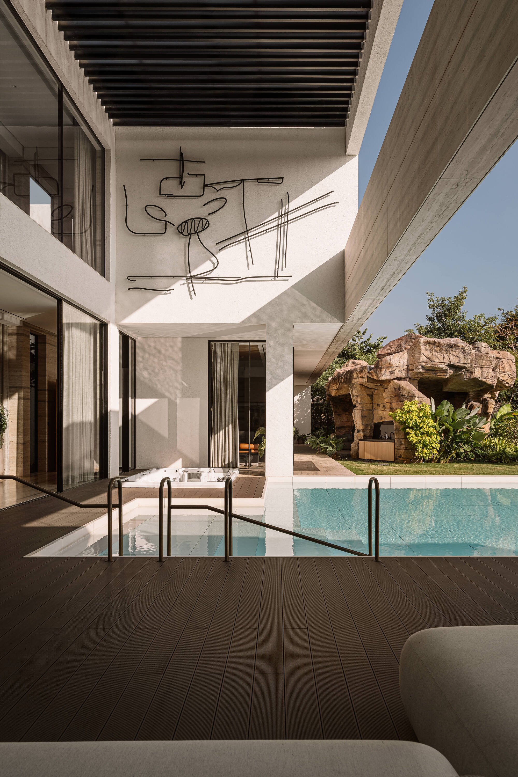 Wire-line mural on a white wall above a pool and timber deck, with a rock grotto beyond in sunlight