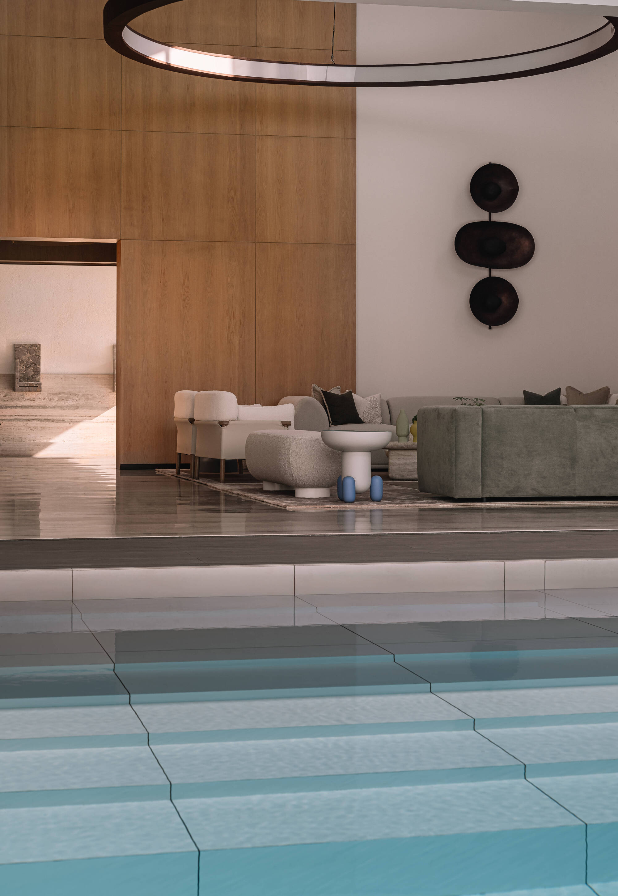 Stepped pool edge in the foreground facing a raised lounge with grey sofas and a stack of dark disc sculptures on the wall