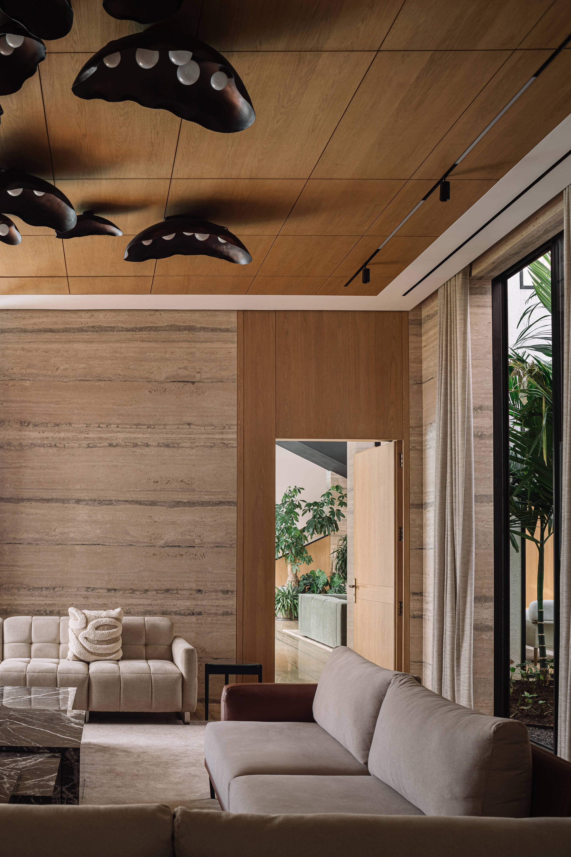 Timber ceiling with clustered black pendant lights above a quilted sofa, with an open door leading to a planted courtyard