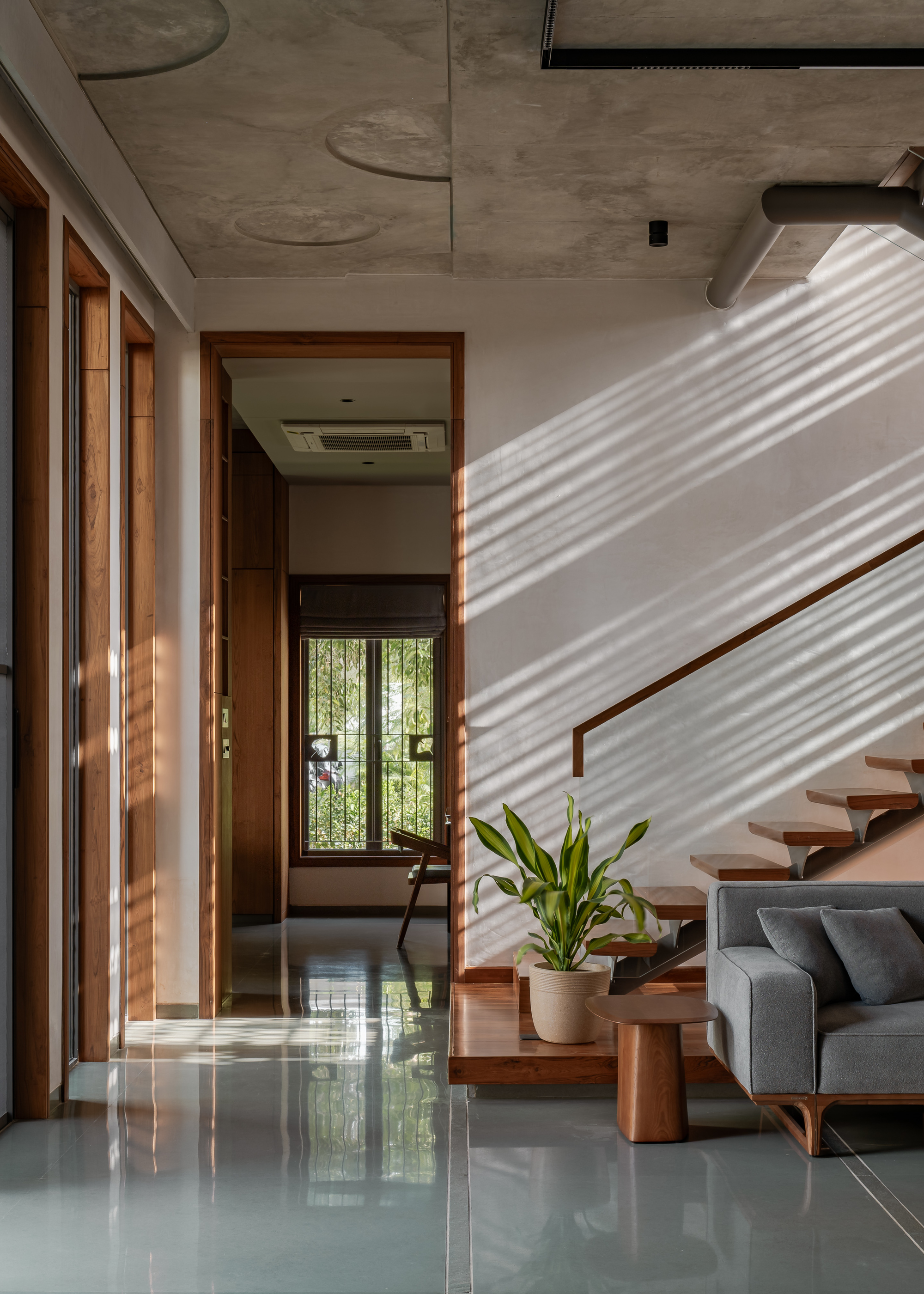 Interior corridor with timber door frames, a potted plant beside the stair and glossy grey floor catching afternoon light