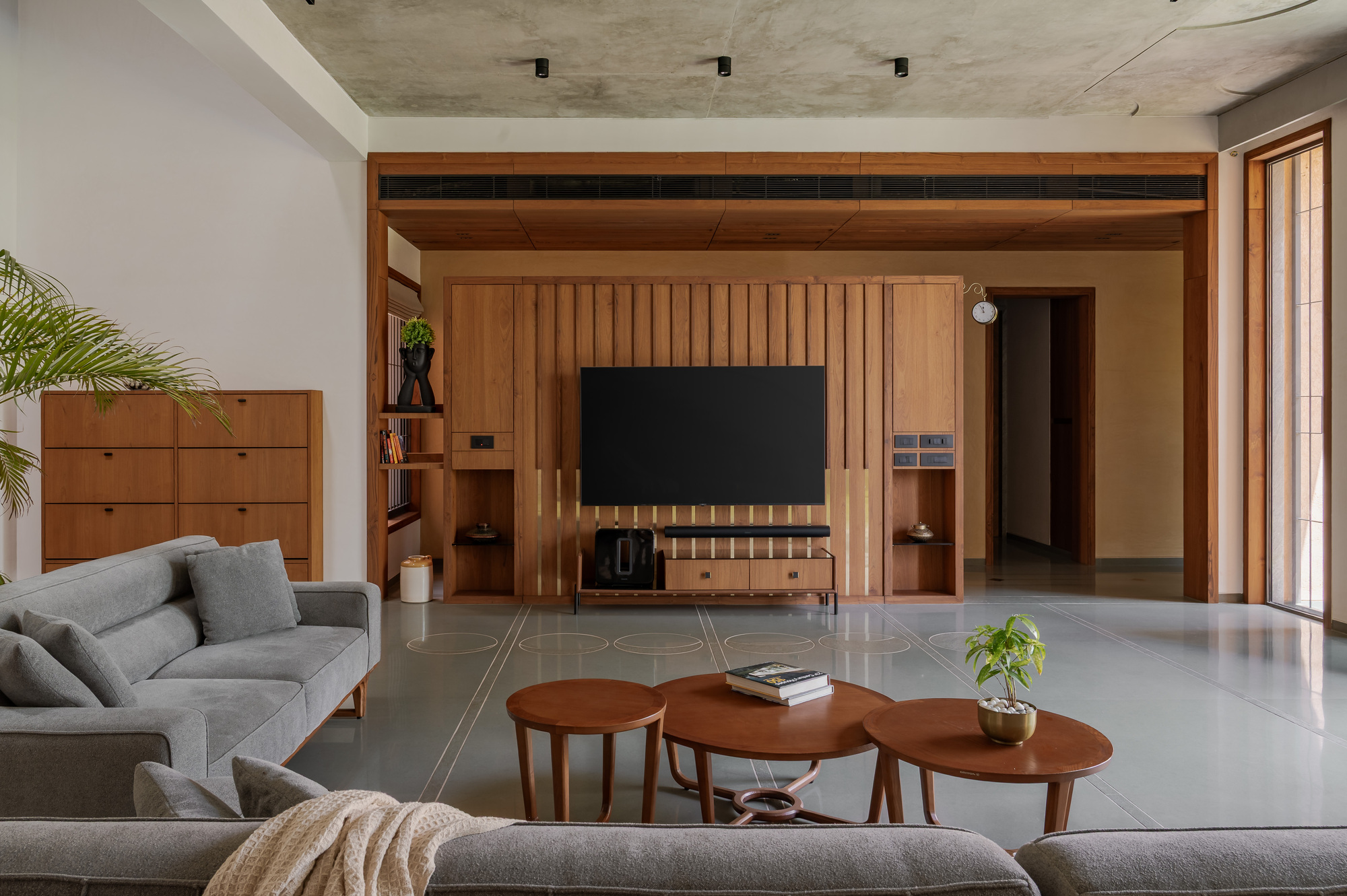 Living room with a timber-framed television wall, grey sofa and round wooden coffee tables on a polished floor with inlaid lines