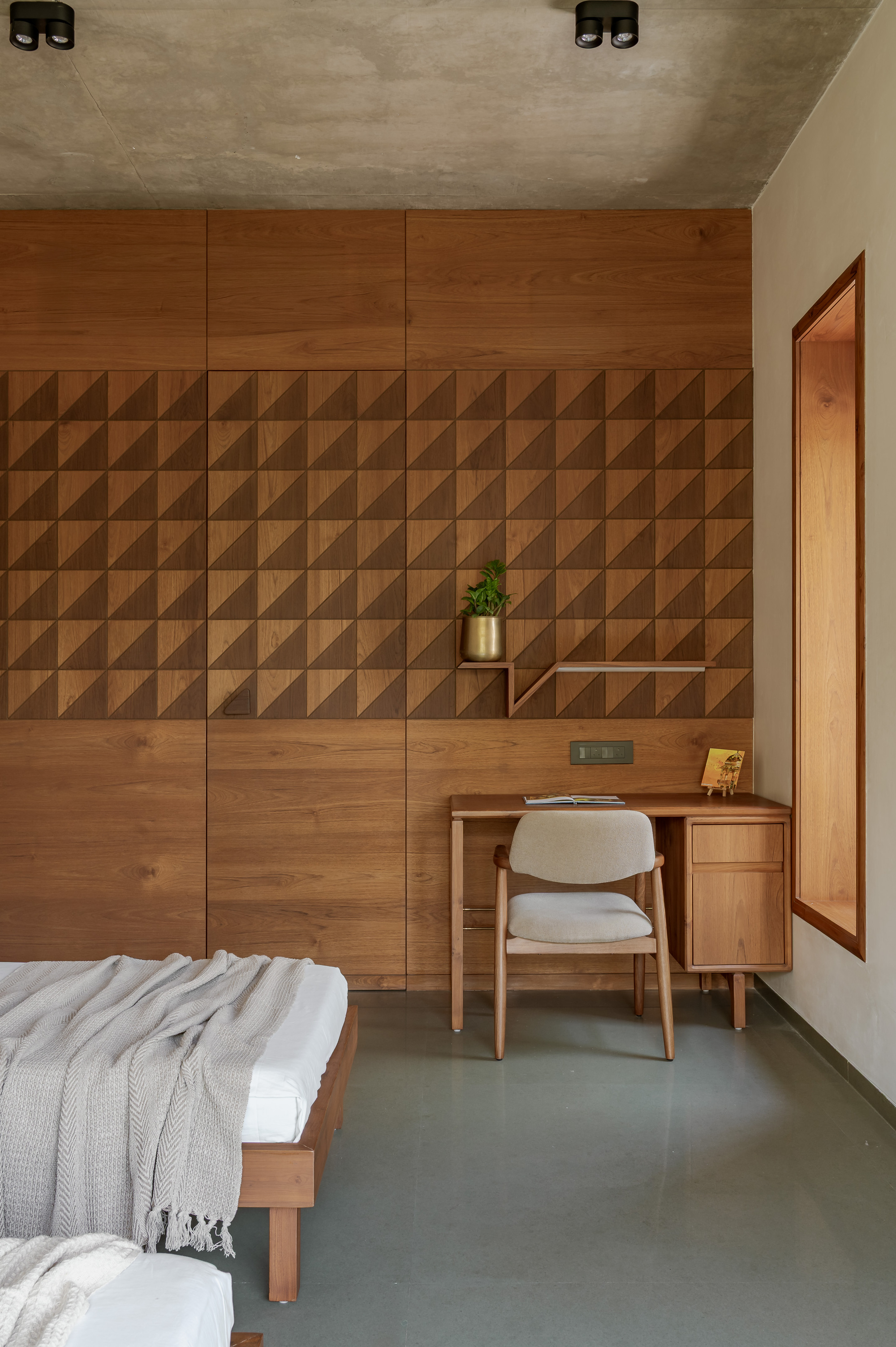 Bedroom wall clad in faceted timber triangles above a built-in desk and chair, with a deep wooden window recess beside it