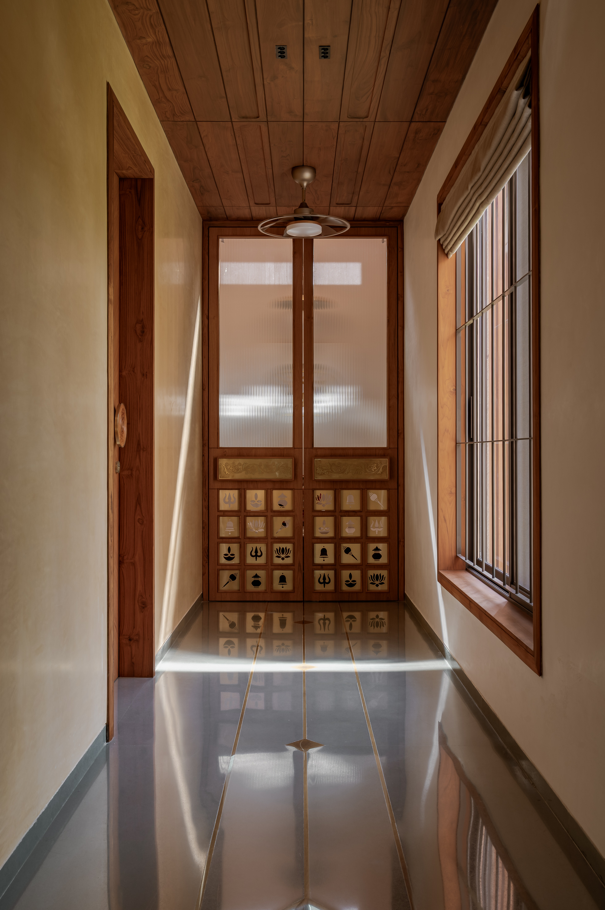Narrow corridor ending in a timber door with frosted glass and inlaid symbols, a shaft of sunlight crossing the polished floor