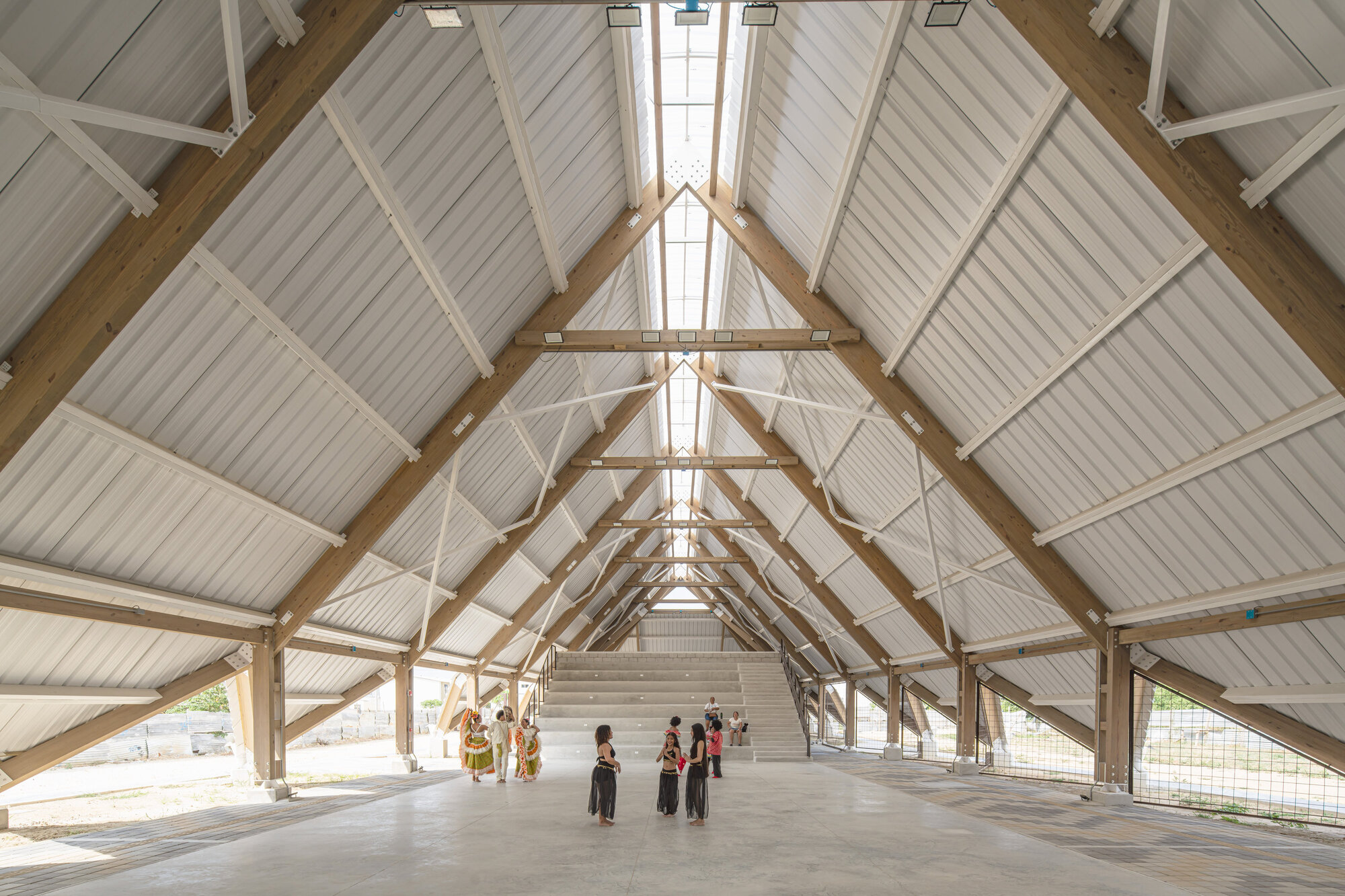 Interior of the timber-framed hall with angled beams, corrugated sheeting and a central skylight, with a small group gathered near the steps