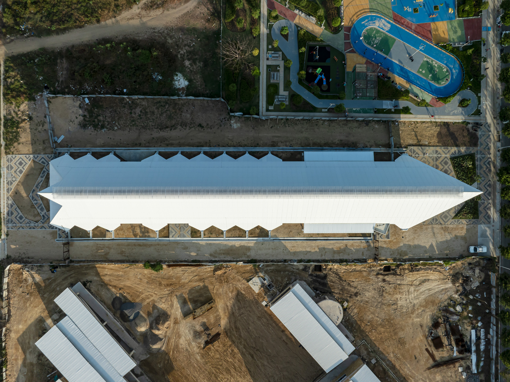 Overhead view of the long white roof with zigzag edges, patterned paving at both ends and a playground above