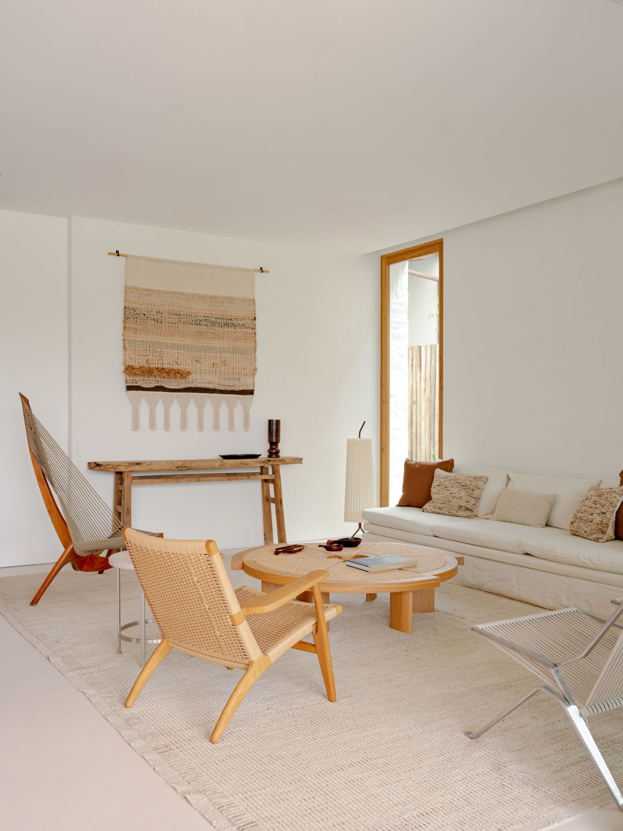Living room corner with rope-seat wooden chairs, a round low table and a woven wall hanging above a rustic console