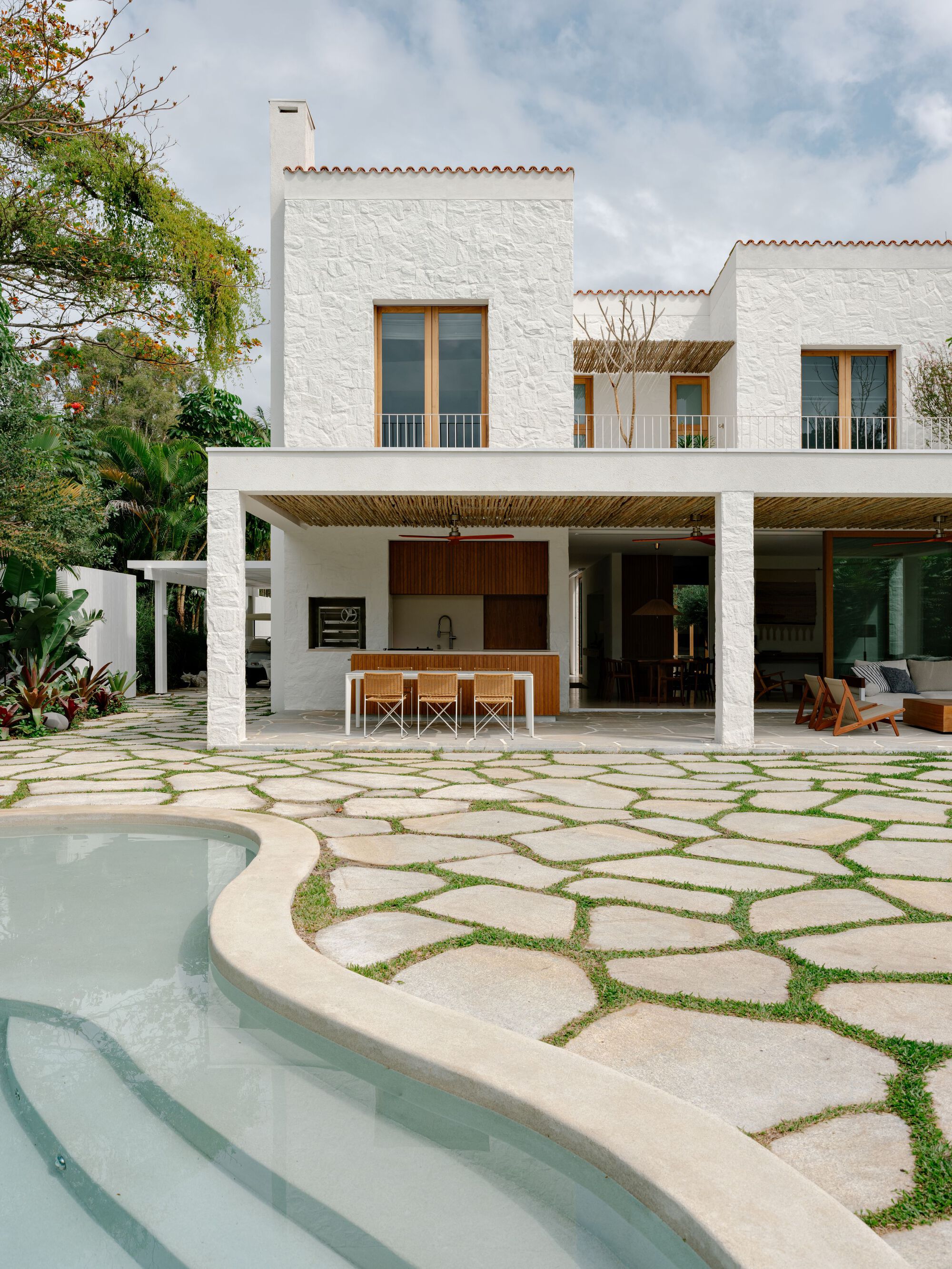 Pool steps and curved coping beside the white porch columns, kitchen counter with stools and bamboo-lined ceiling