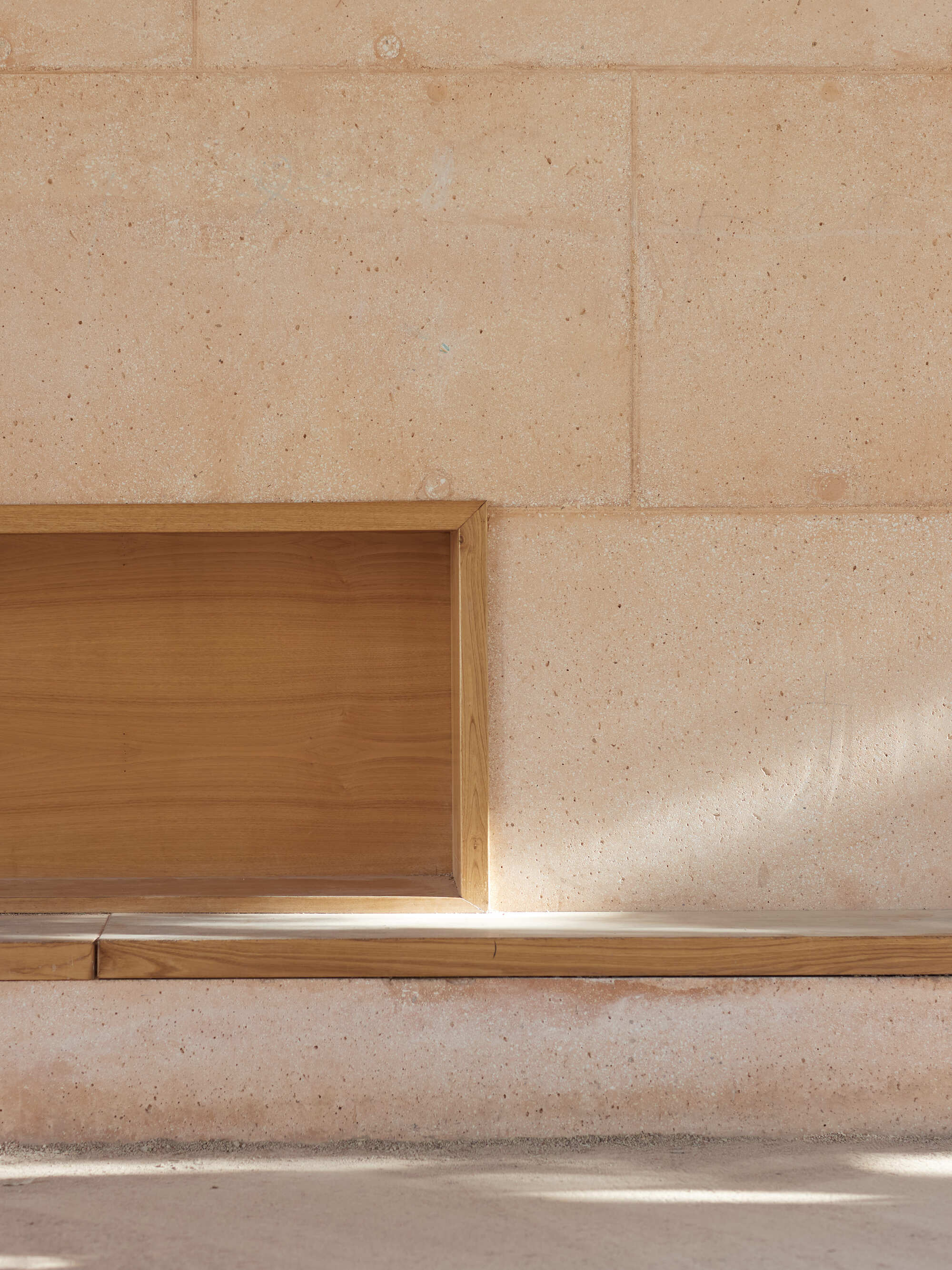 Close-up of a timber-framed niche above a wooden bench ledge set into the block wall, with a sliver of sunlight