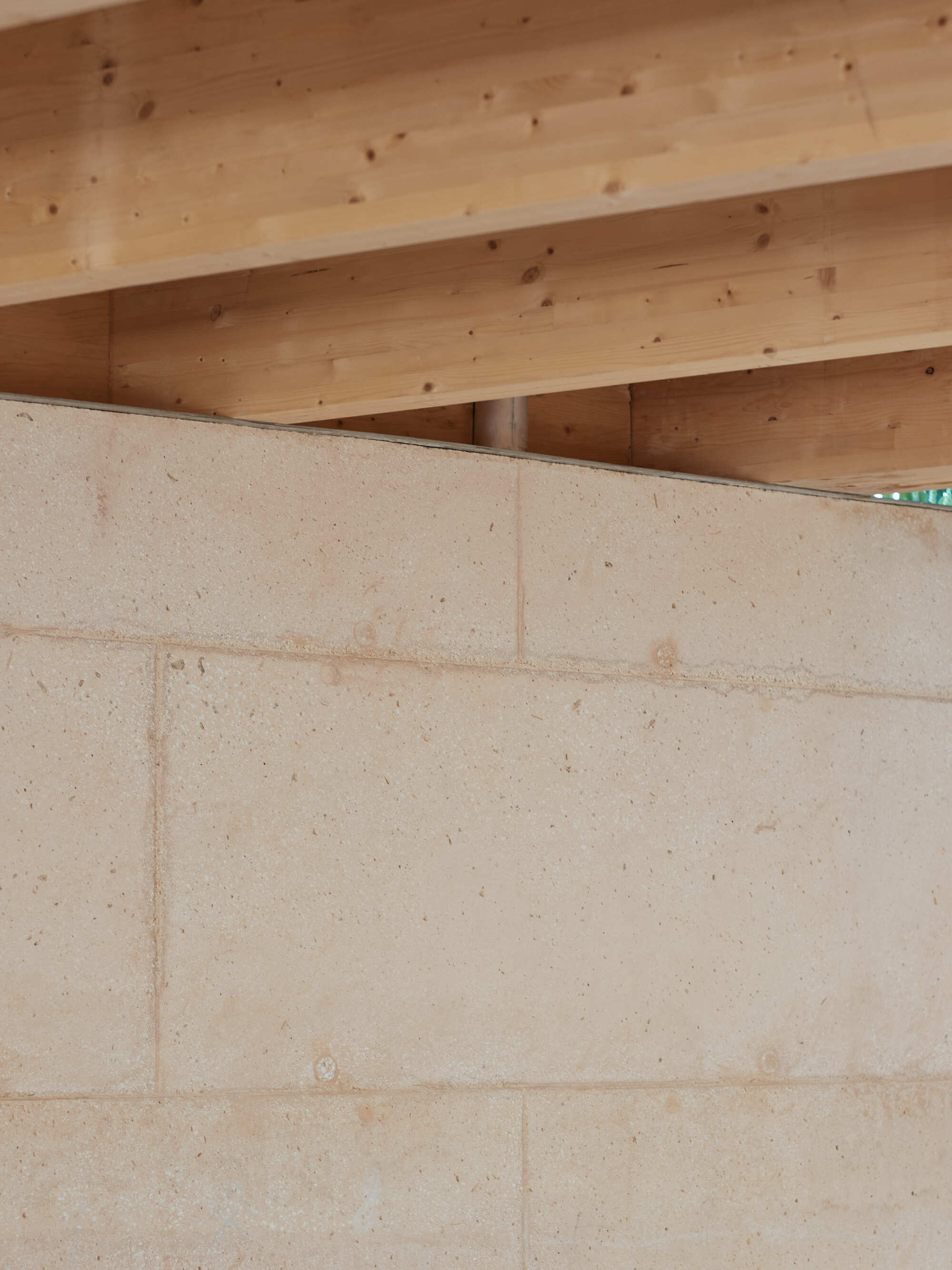 Glulam roof beams resting on top of the sand-coloured block wall, seen from below in soft daylight