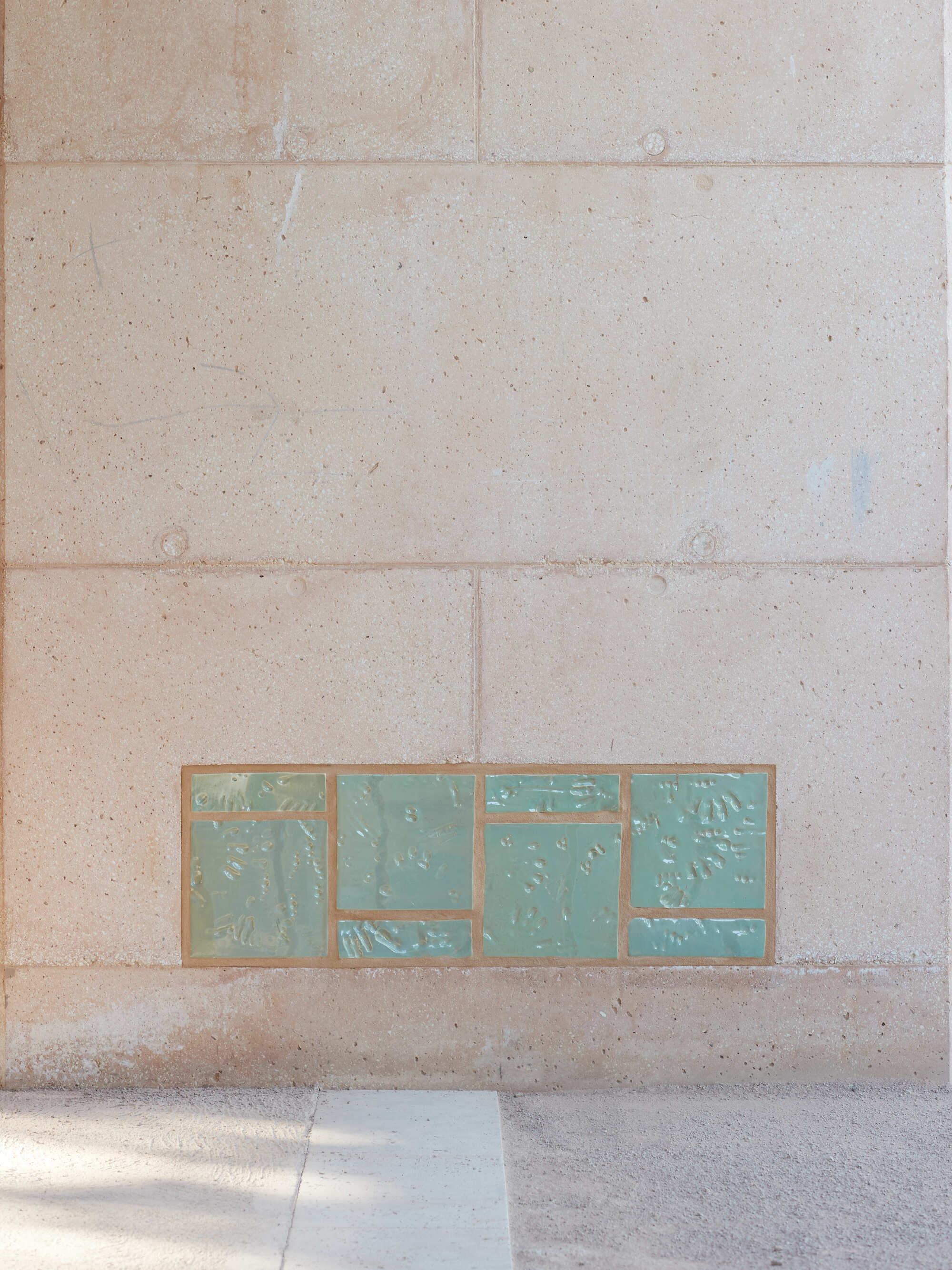 Recessed panel of green glazed ceramic tiles set low in the pale block wall beside a paved floor edge