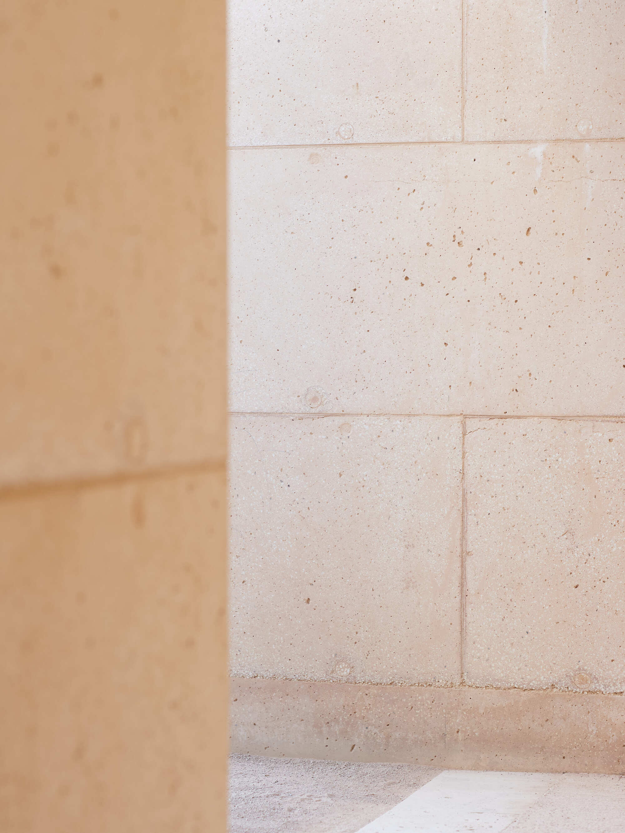 Soft-focus corner of a block wall seen past a blurred earthen column, with bright light on the floor
