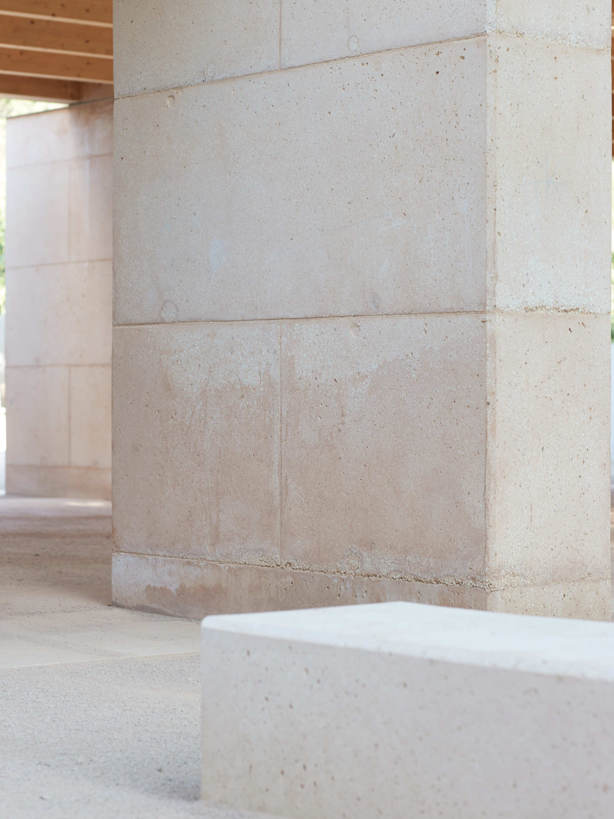 Stacked block column with visible horizontal joints and a pale stone bench in the foreground, timber ceiling behind