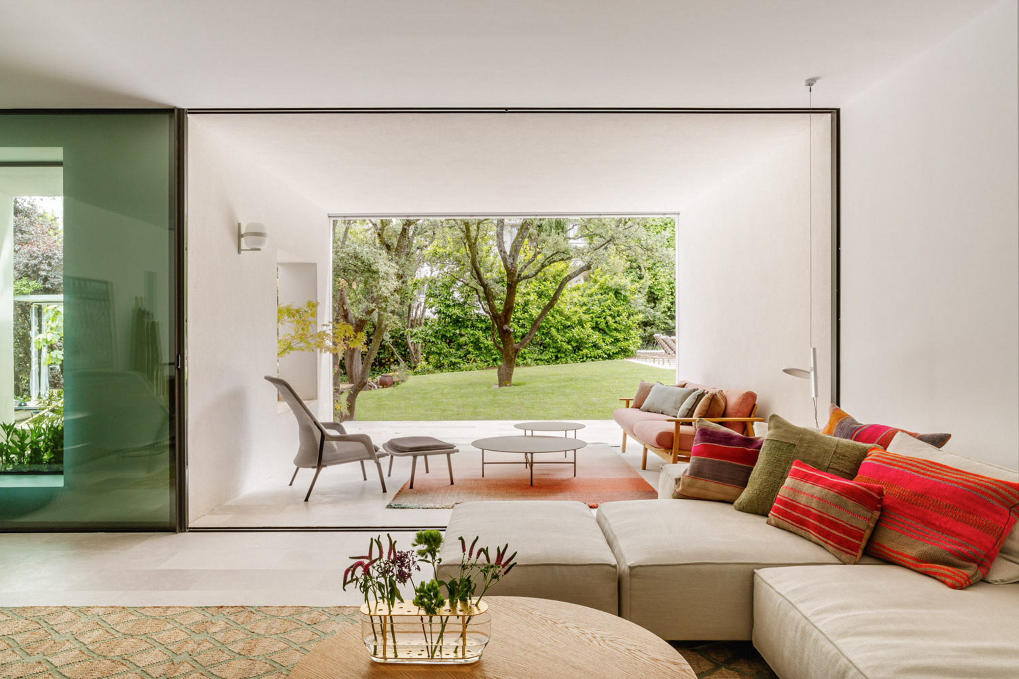 Living room with cream sofa and striped cushions opening through a large frame to a covered terrace and oak trees