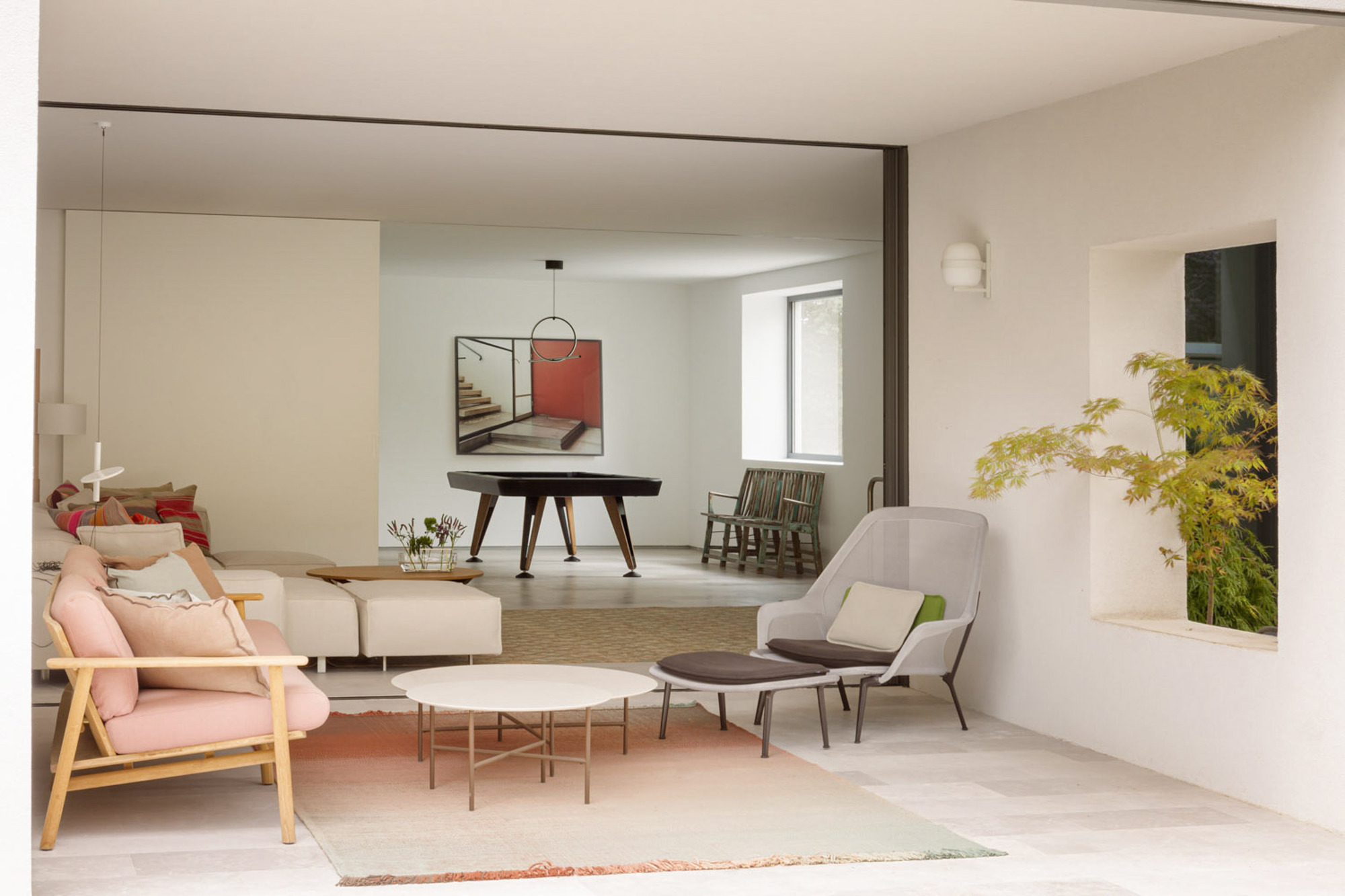 Sitting area with a pink armchair and round table opening to a billiard room, a potted maple glowing in a wall niche