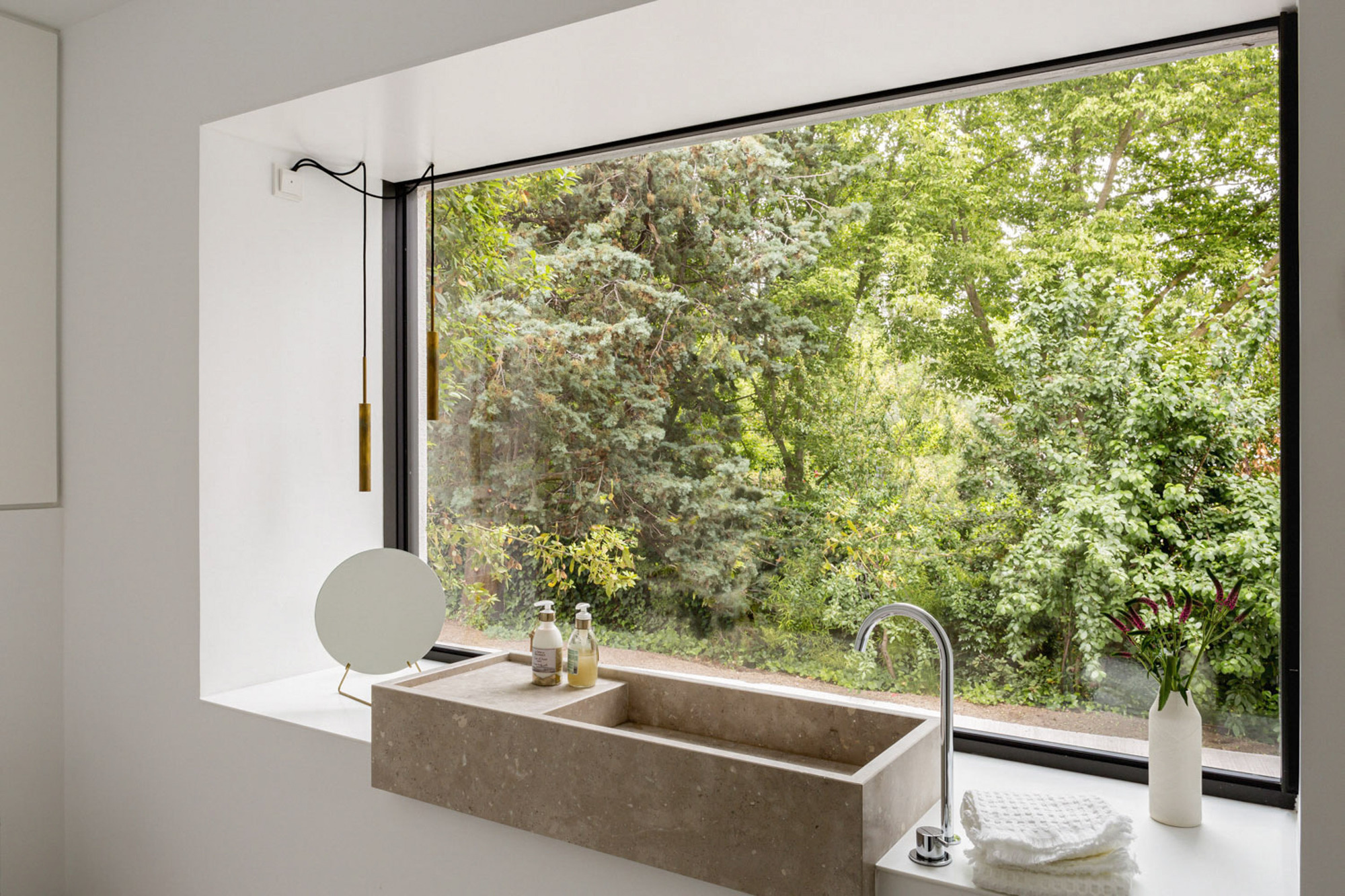 Stone basin with a curved tap set in a deep window recess facing dense green trees