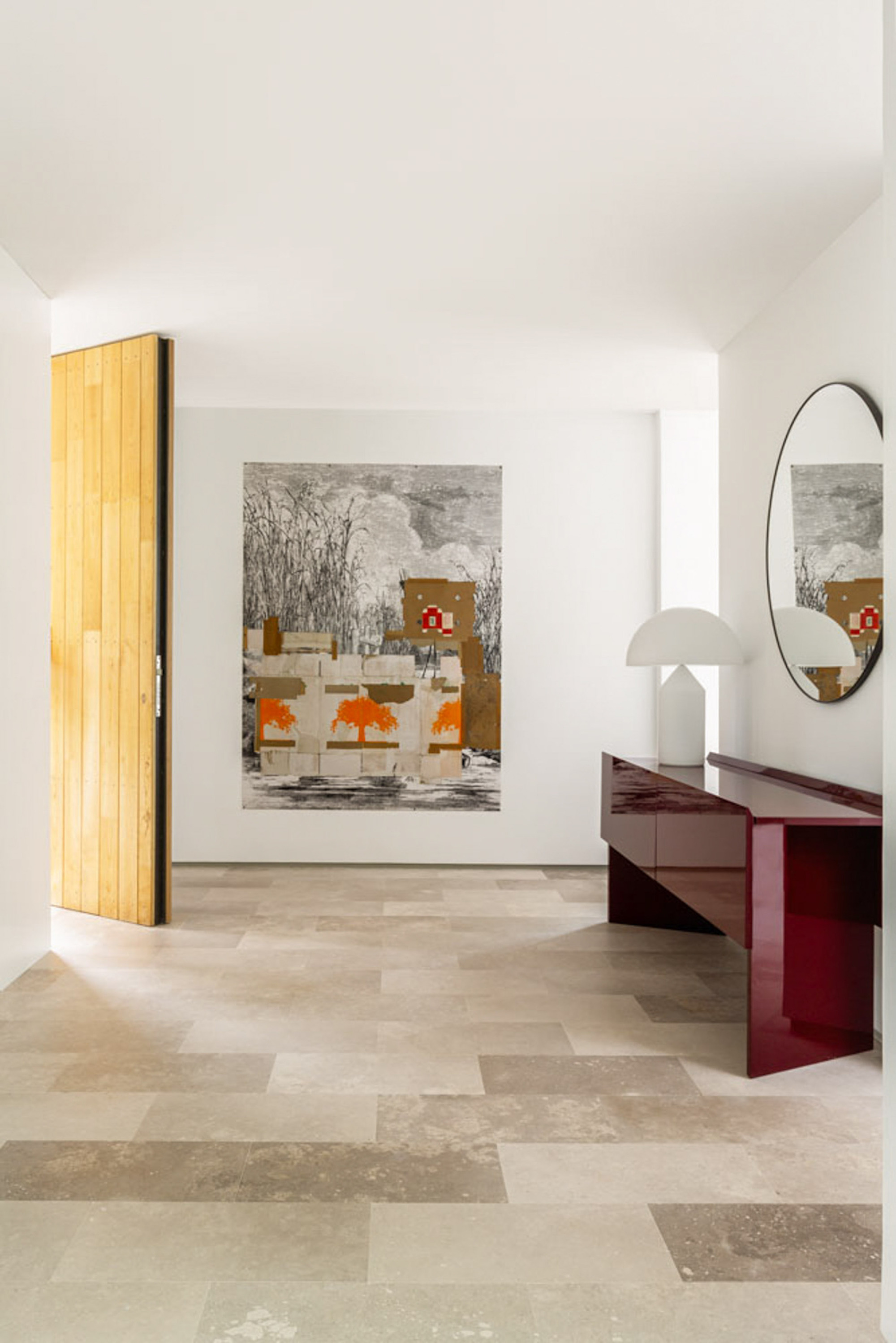 Entry hall with a tall pivot door, large framed artwork and a maroon lacquered console on a limestone floor