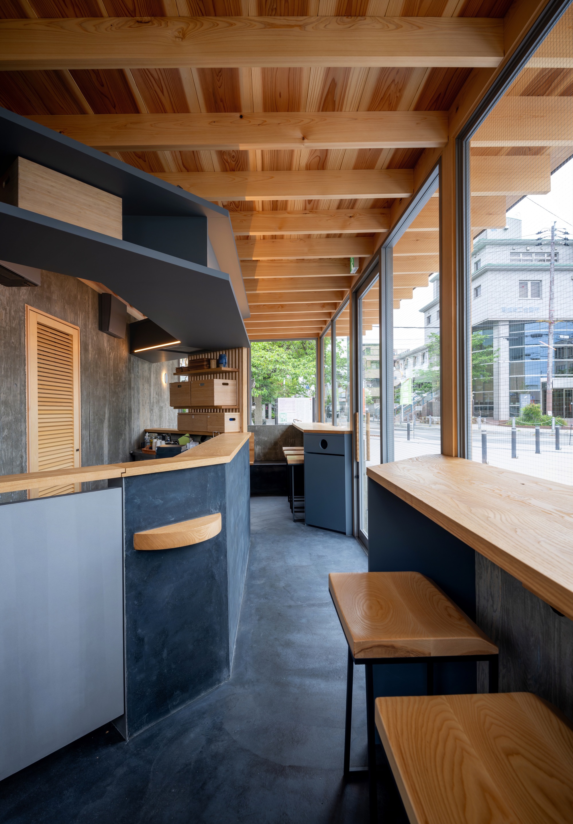 Interior of the narrow kiosk with a counter, timber ceiling slats and a window bar with wooden stools facing the street