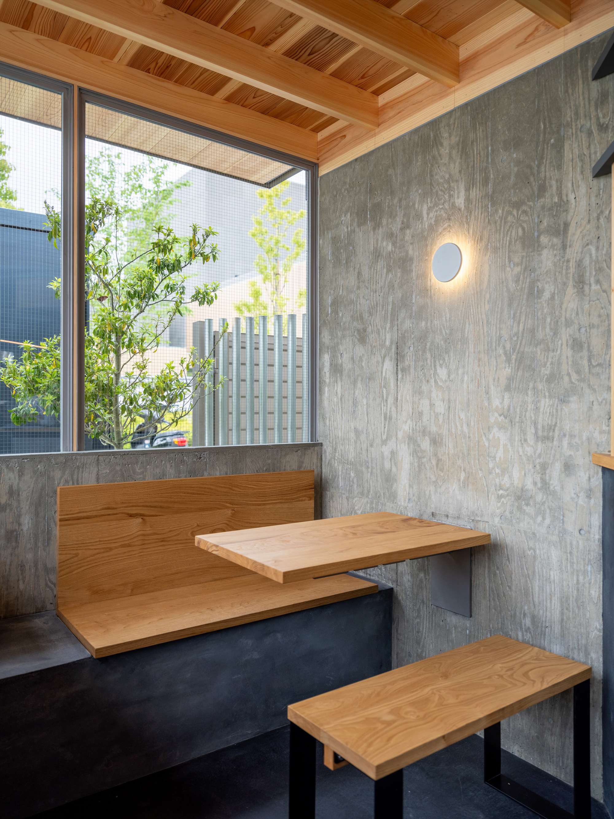 Corner seating nook with a wooden bench, fold-out table and board-formed concrete wall lit by a round wall lamp