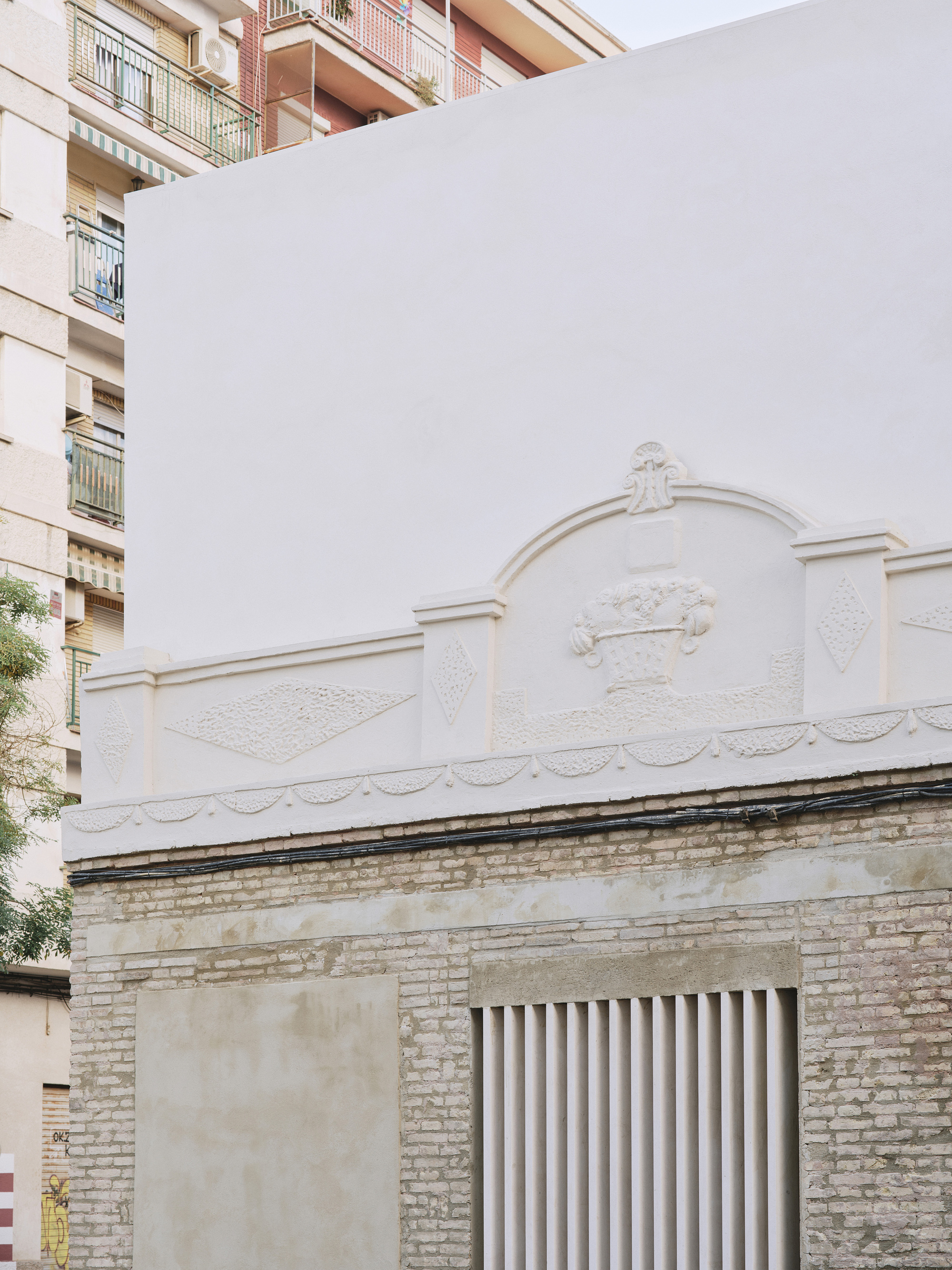 Street corner view of the ornamented plaster parapet and brick base, with apartment balconies and a tree behind