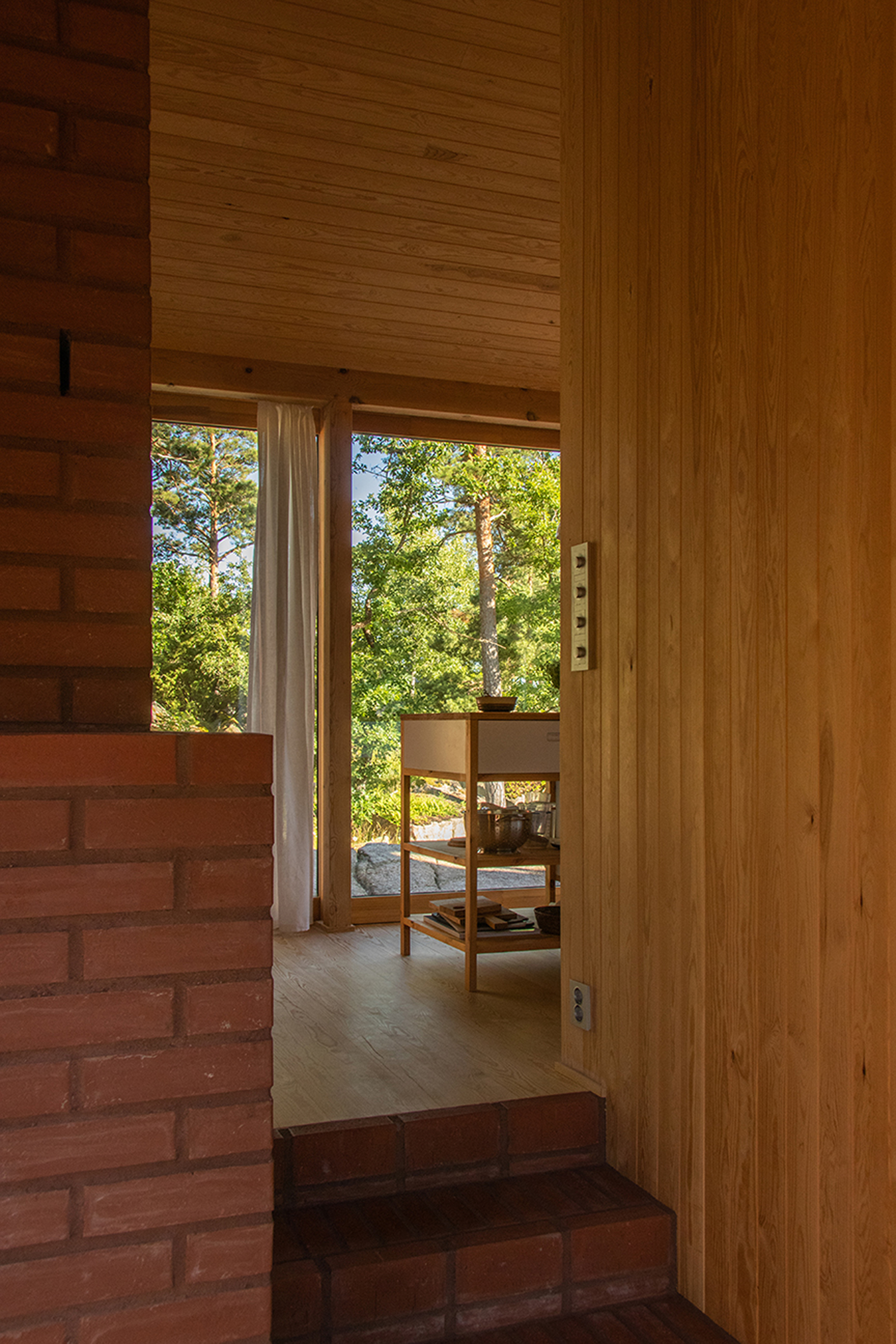Doorway view past a brick wall and brick steps to a kitchen cart and linen curtain in afternoon light