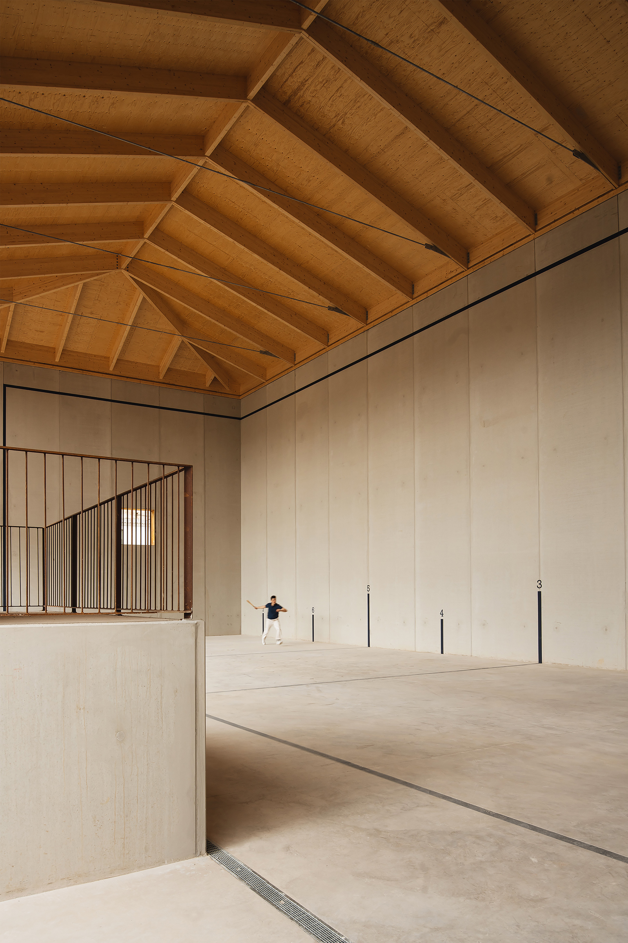 Interior of a court hall with a timber hip roof, concrete panel walls and a lone player on the floor