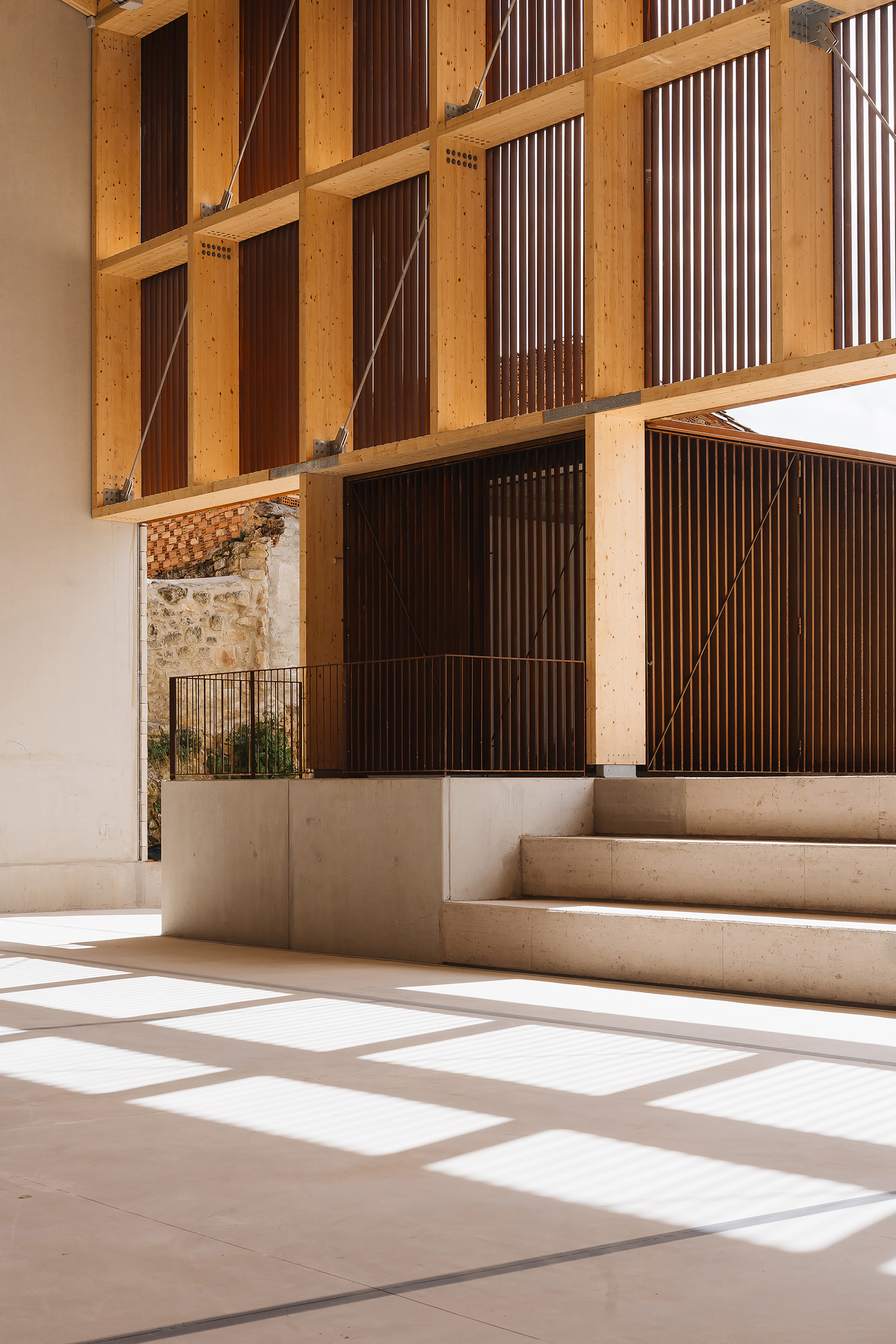 Close view of the timber slat screen above a concrete plinth and stepped seating, with sunlight patches on the floor