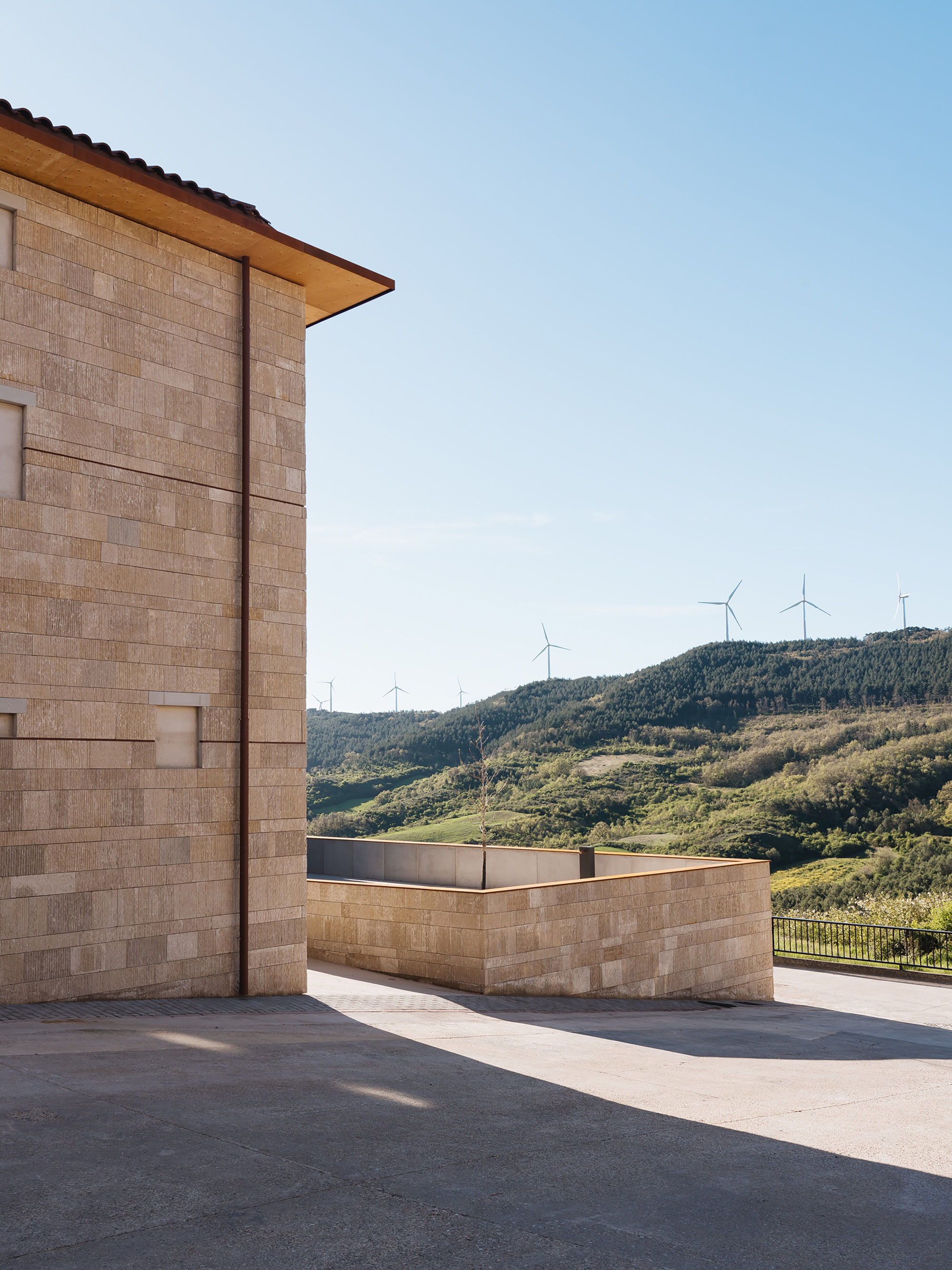 Stone block corner with copper downpipe and deep eaves, overlooking green hills and distant wind turbines in clear morning light