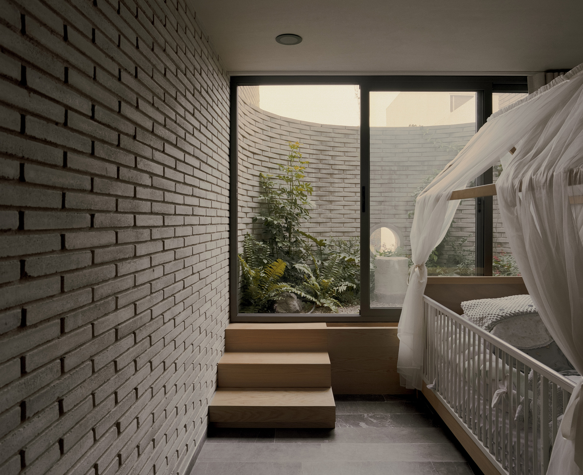 Child's room with a canopied cot and oak steps rising to a window onto a curved brick courtyard with ferns